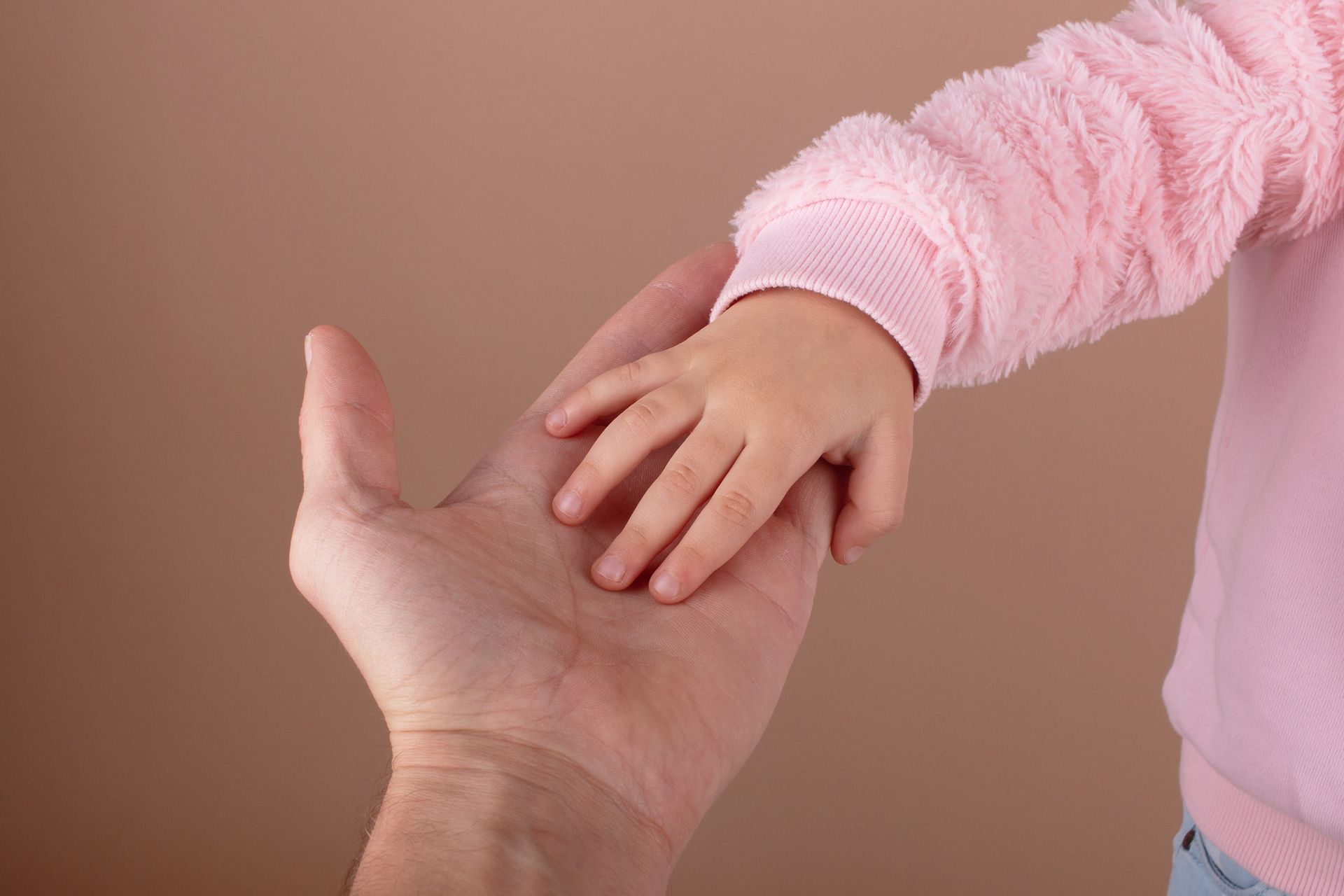 Adult hand holding a child's small hand, both are pale-skinned. Child wears a pink sweater. Adult hand holding a child's small hand, both are pale-skinned. Child wears a pink sweater.