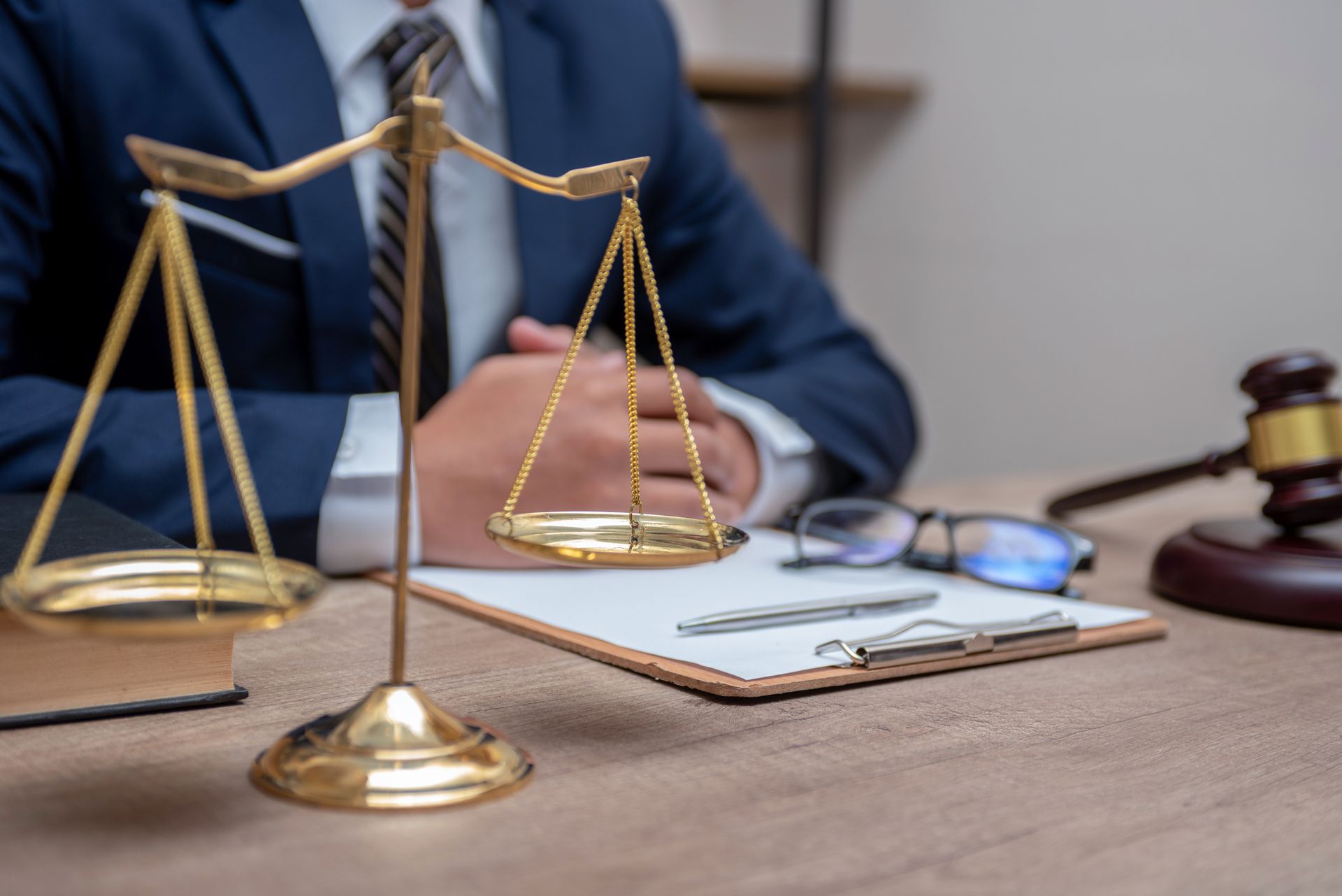 Scales of justice, legal documents, and gavel on a desk with a person in a suit, suggesting legal counsel.