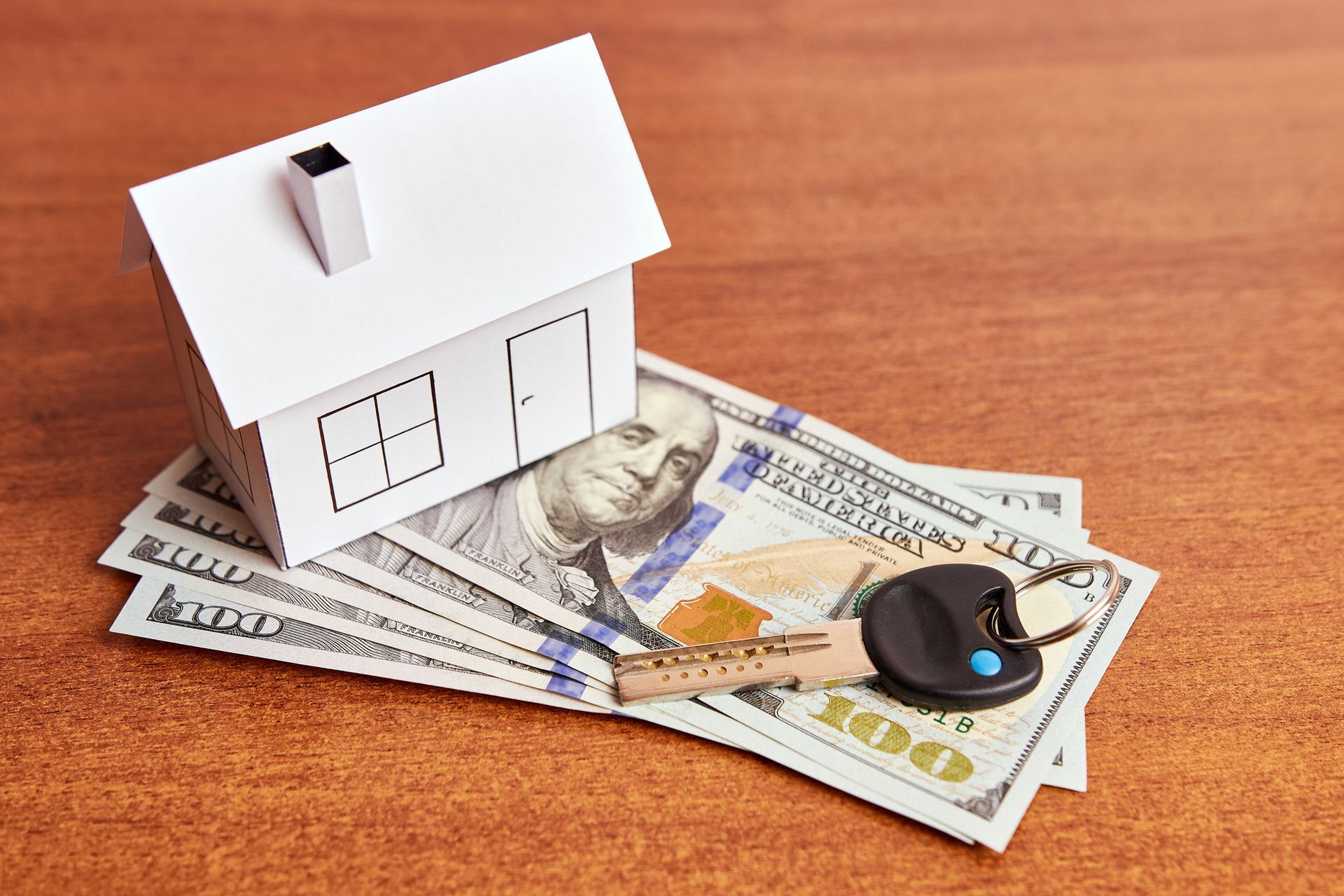 White model house, US currency, and keys on a wooden surface. White model house, US currency, and keys on a wooden surface.