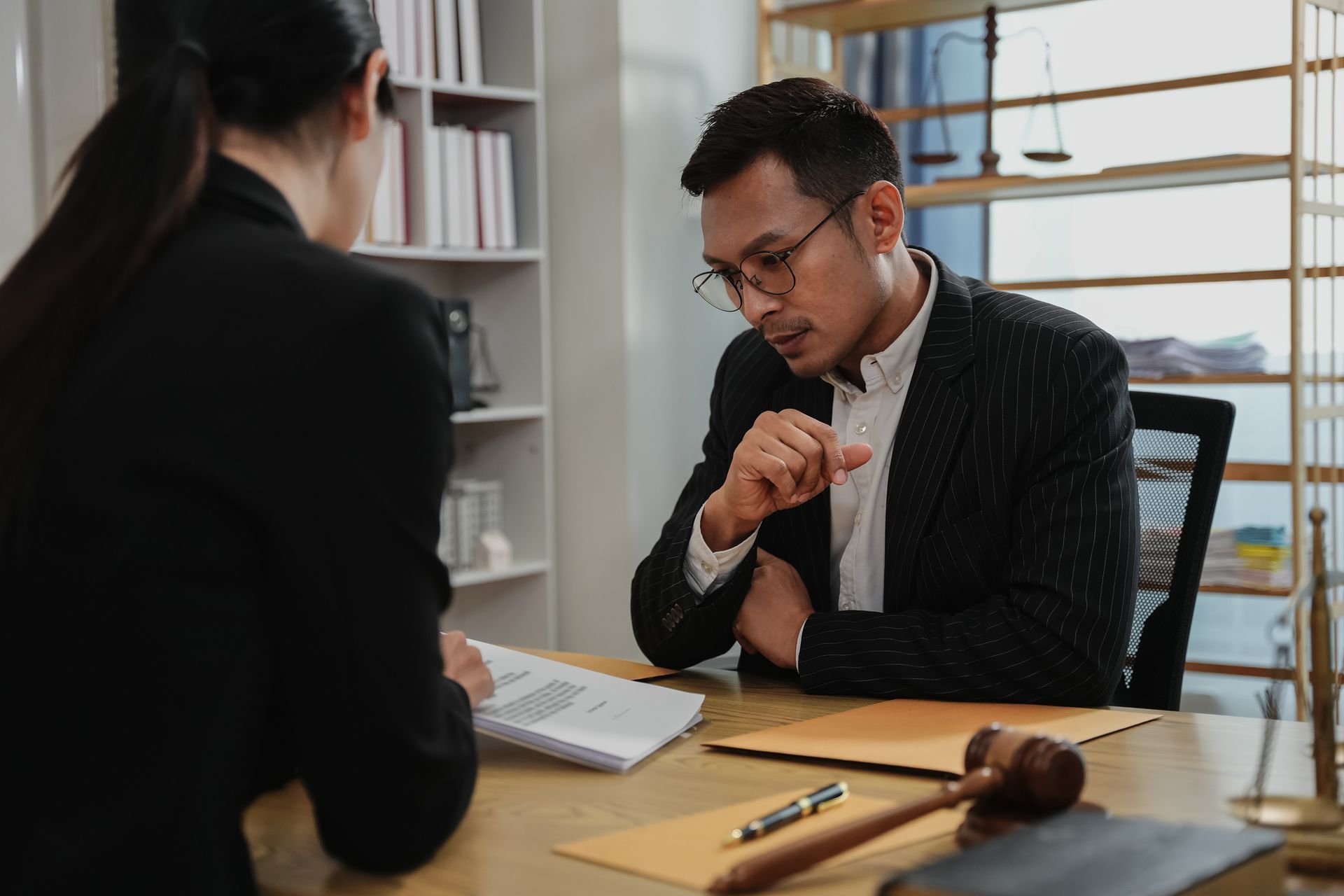Lawyer and client review documents at a desk in an office. Gavel and scale visible.