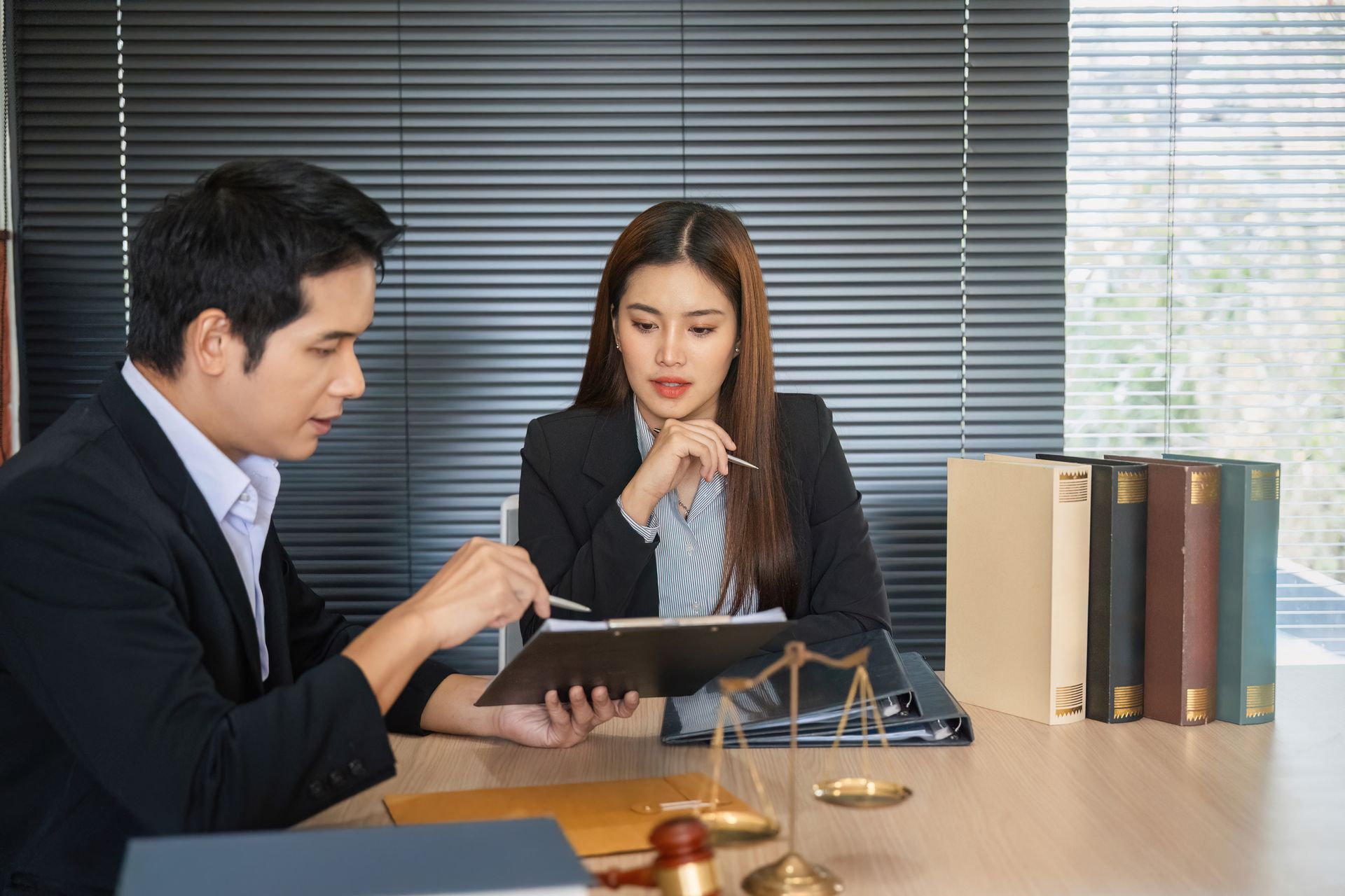 Two people in business attire reviewing documents at a desk in an office setting. Two people in business attire reviewing documents at a desk in an office setting.