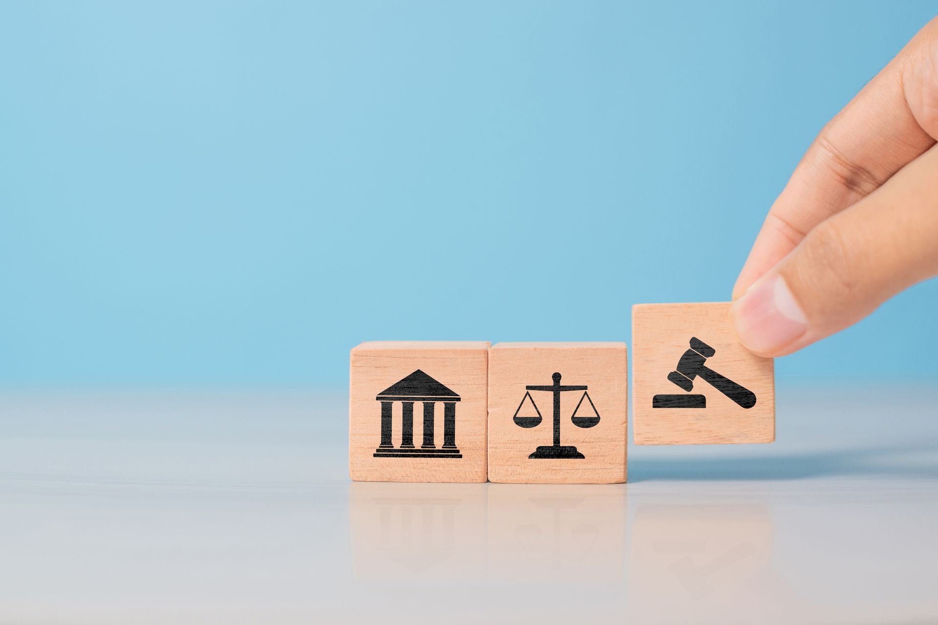 Hand placing a gavel symbol block next to blocks with courthouse and scales of justice symbols. Hand placing a gavel symbol block next to blocks with courthouse and scales of justice symbols.