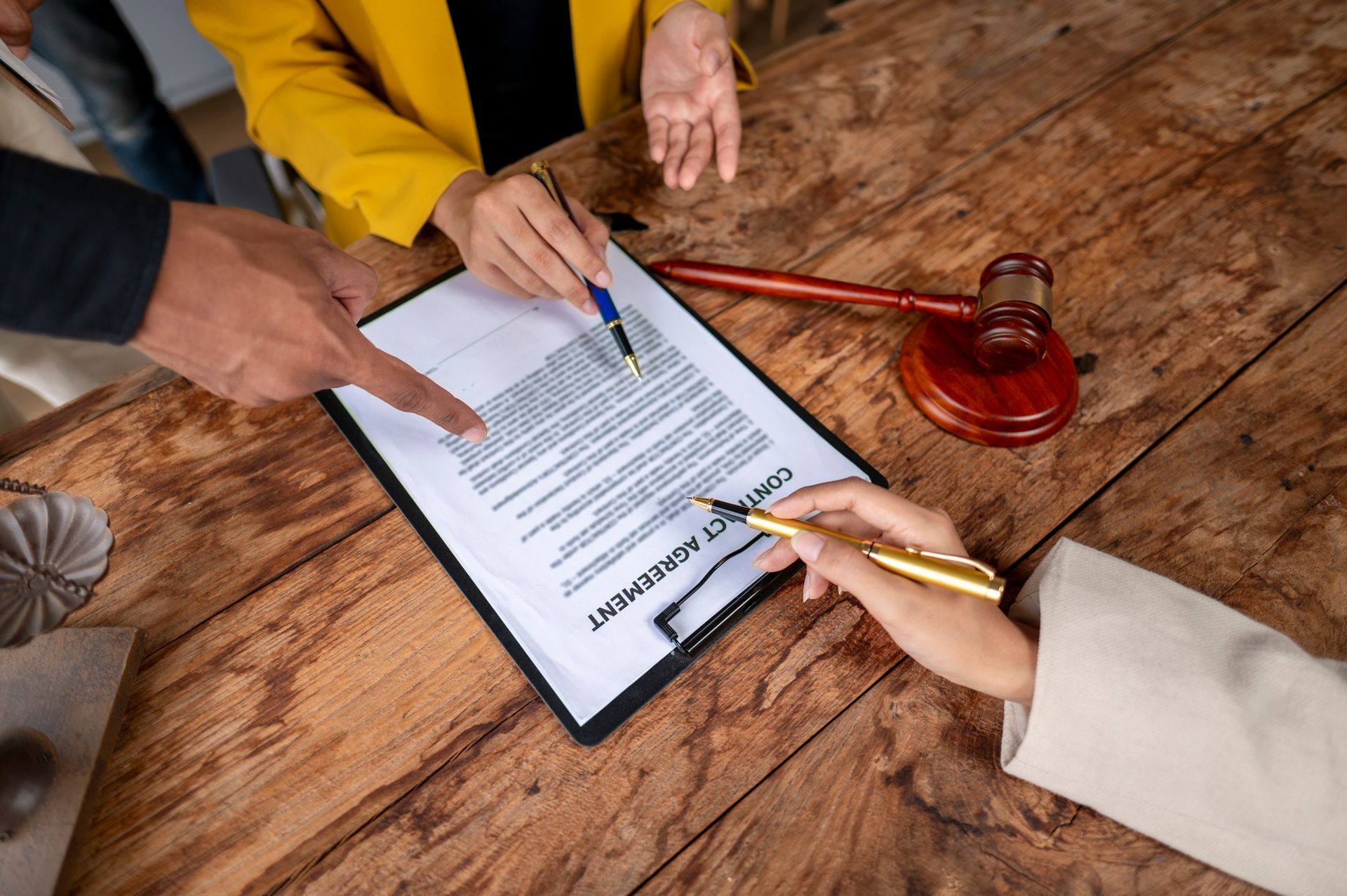People signing a contract at a wooden table, gavel nearby. People signing a contract at a wooden table, gavel nearby.