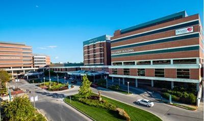 A bright, sunny day at a brick hospital complex featuring the Pellaver Building with a green logo and landscaped grounds.