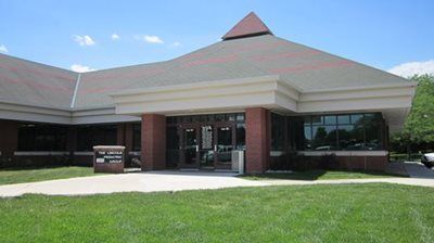A modern one-story brick office building with a pyramid-shaped roof, featuring a central glass entrance and green lawn.