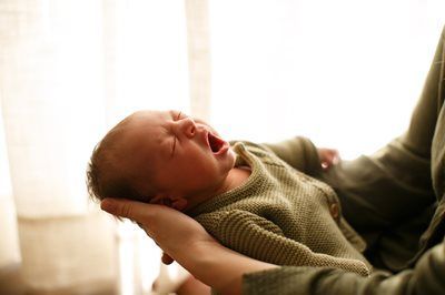 A person holding a newborn who is yawning, set against a bright, softly lit window.