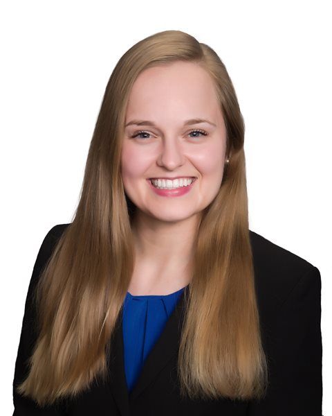 A professional headshot of a smiling person with long light brown hair, wearing a black blazer over a blue top.