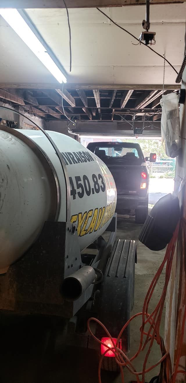 Une bétonnière garée dans un garage avec un camion visible en arrière-plan.