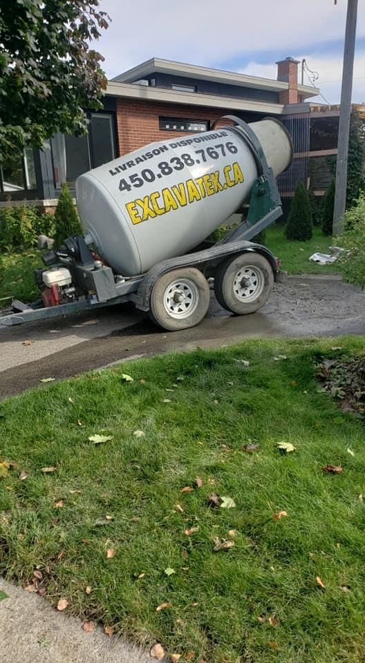 Une bétonnière se trouve sur une remorque devant une maison.