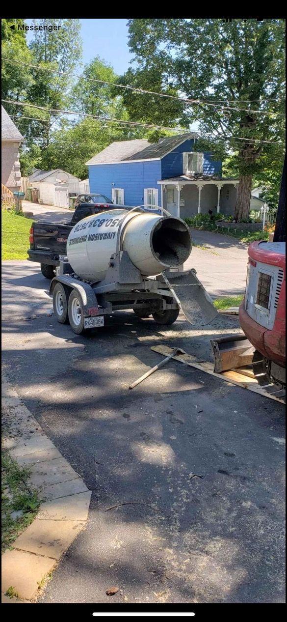 Un camion malaxeur à béton circule dans une rue à côté d’une maison.