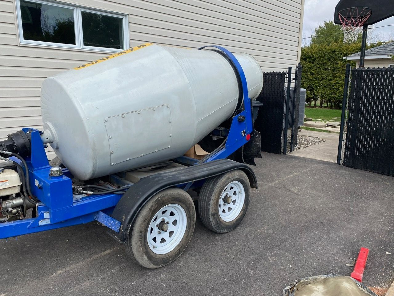 Une bétonnière sur remorque est garée devant une maison.
