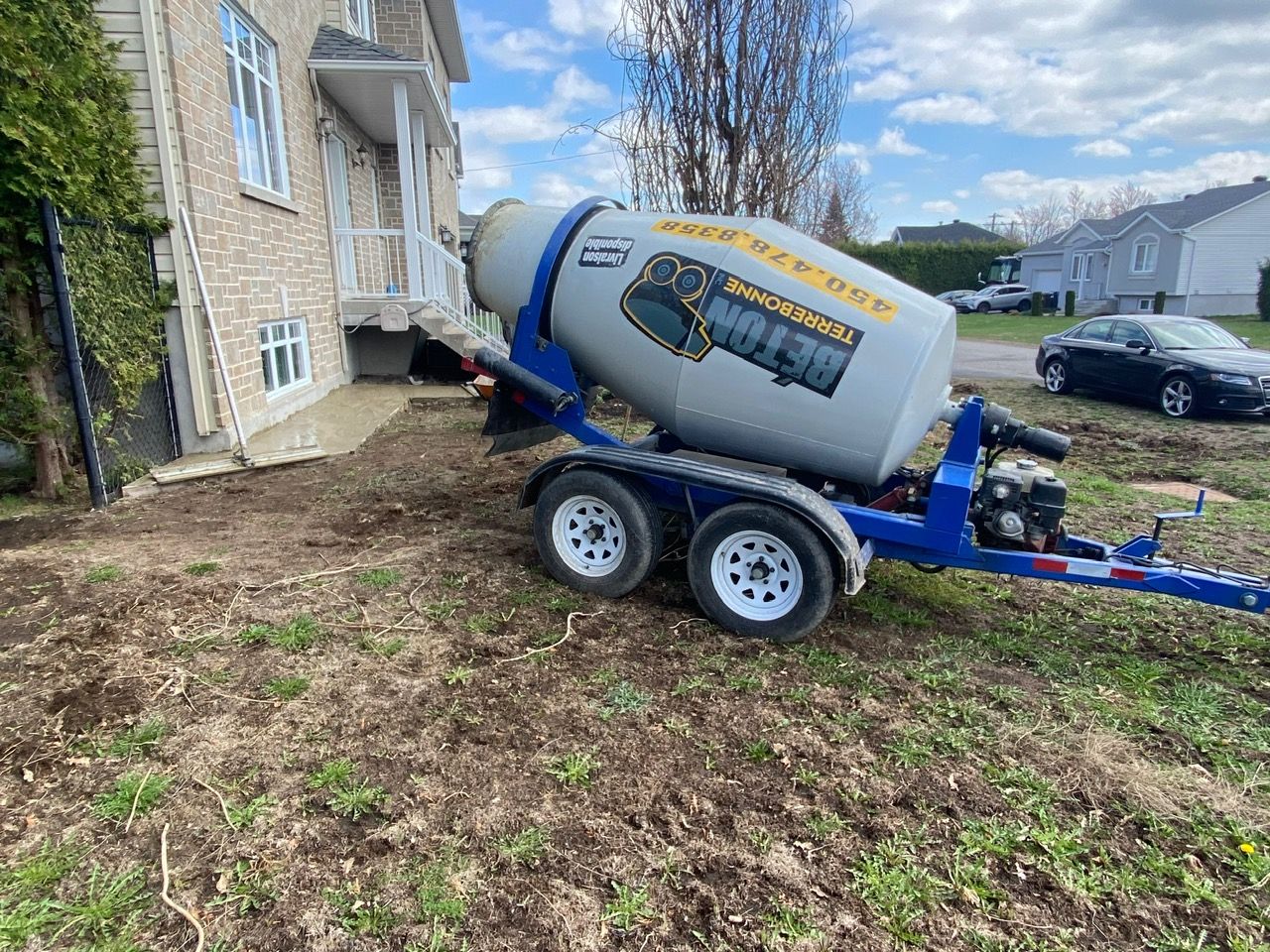 Une bétonnière se trouve sur une remorque devant une maison.