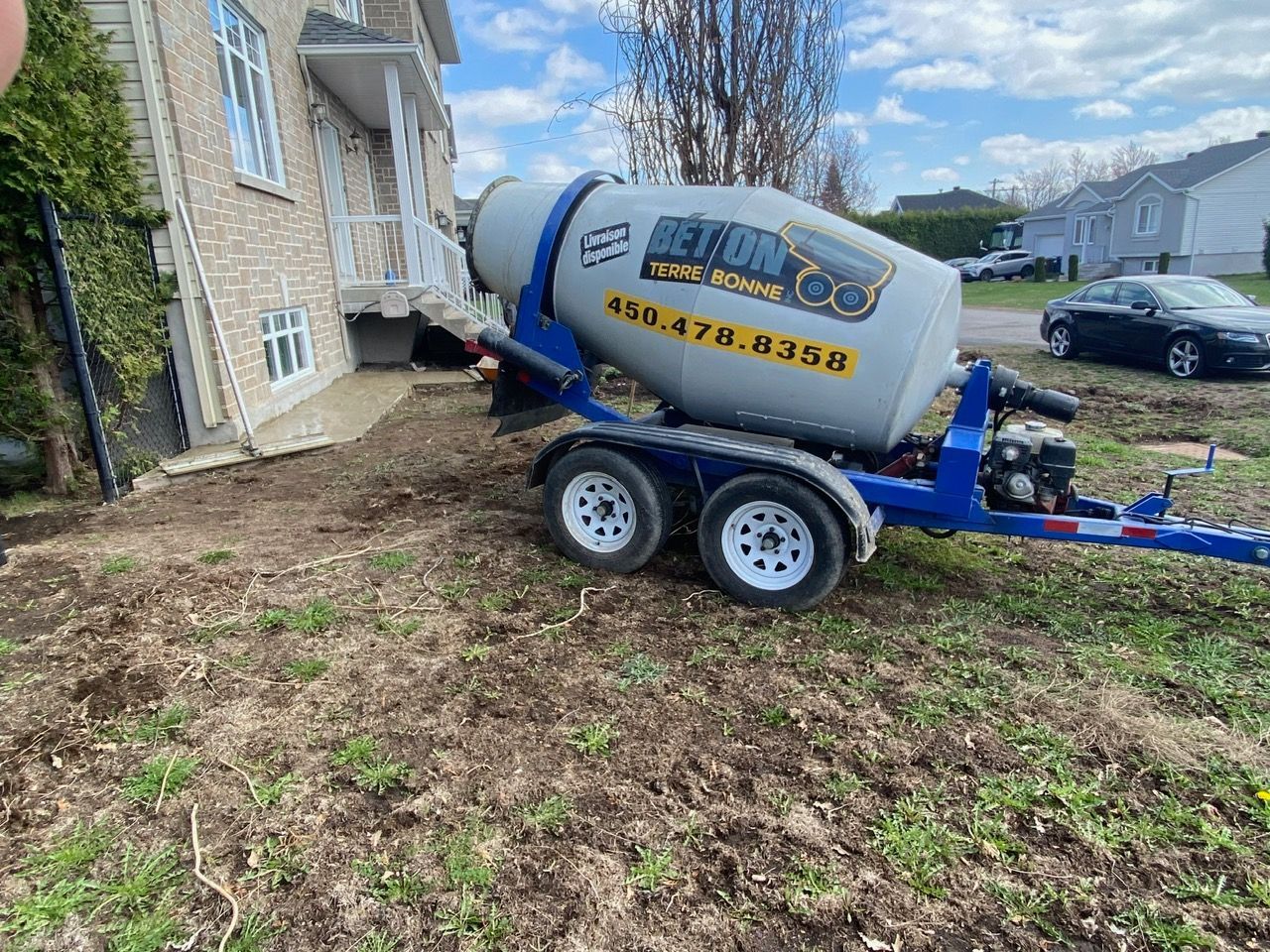 Une bétonnière se trouve sur une remorque devant une maison.