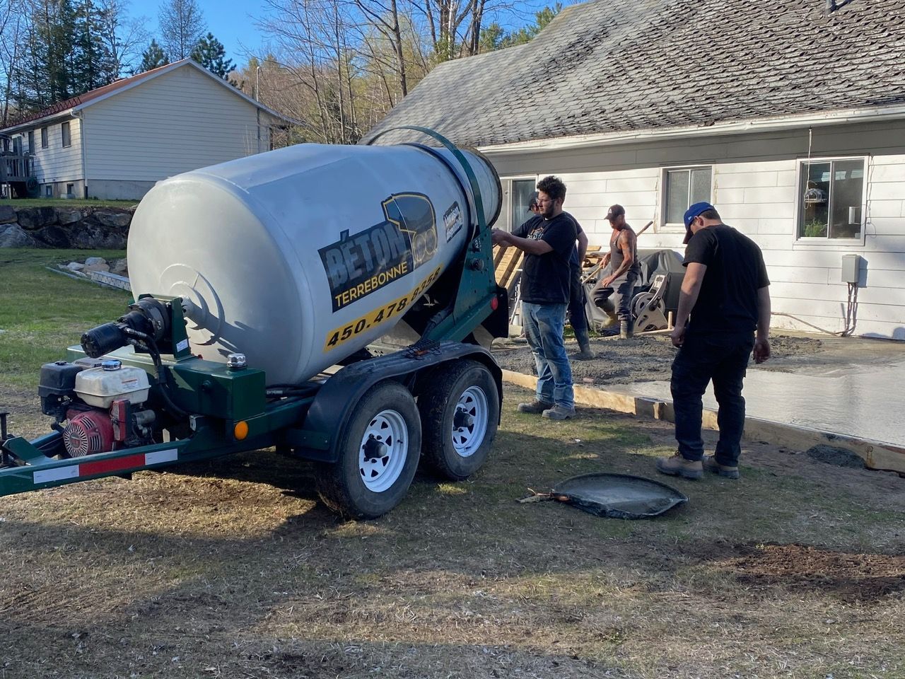 Une bétonnière se trouve sur une remorque devant une maison.