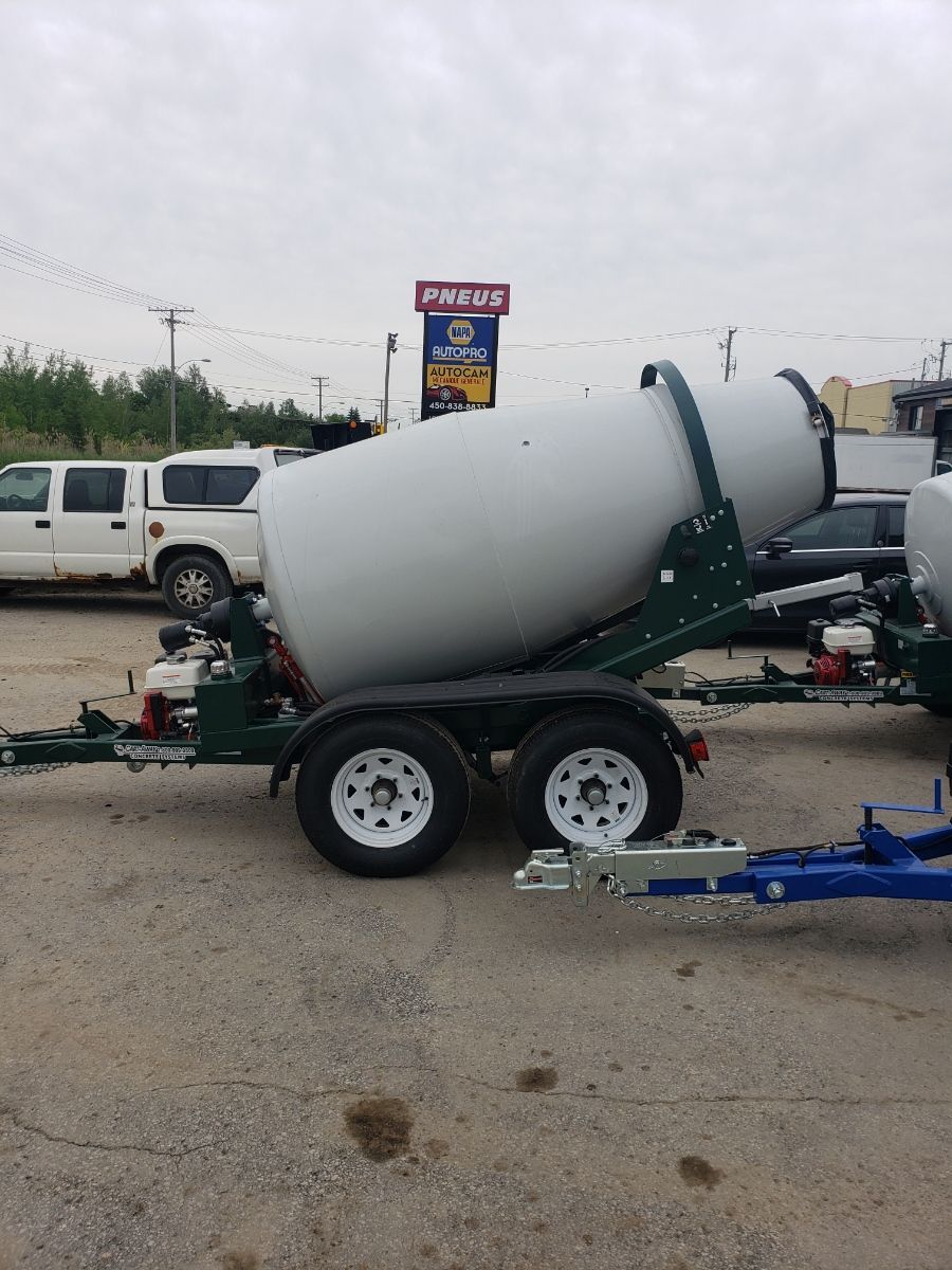 Remorque malaxeur à béton avec tambour blanc, châssis vert et pneus blancs sur un terrain gris.