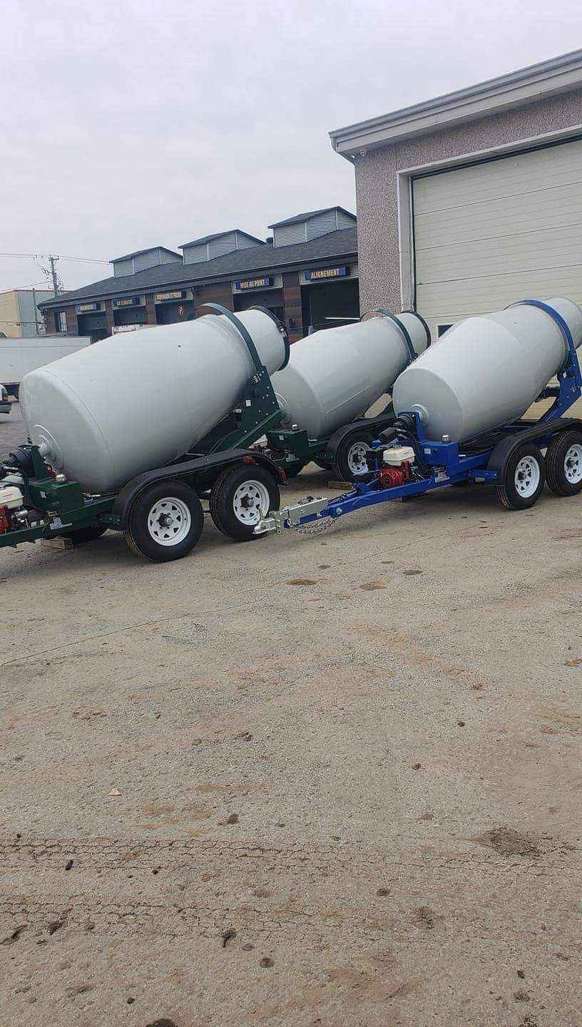 Trois bétonnières, verte et bleue, garées devant un bâtiment sur du gravier.
