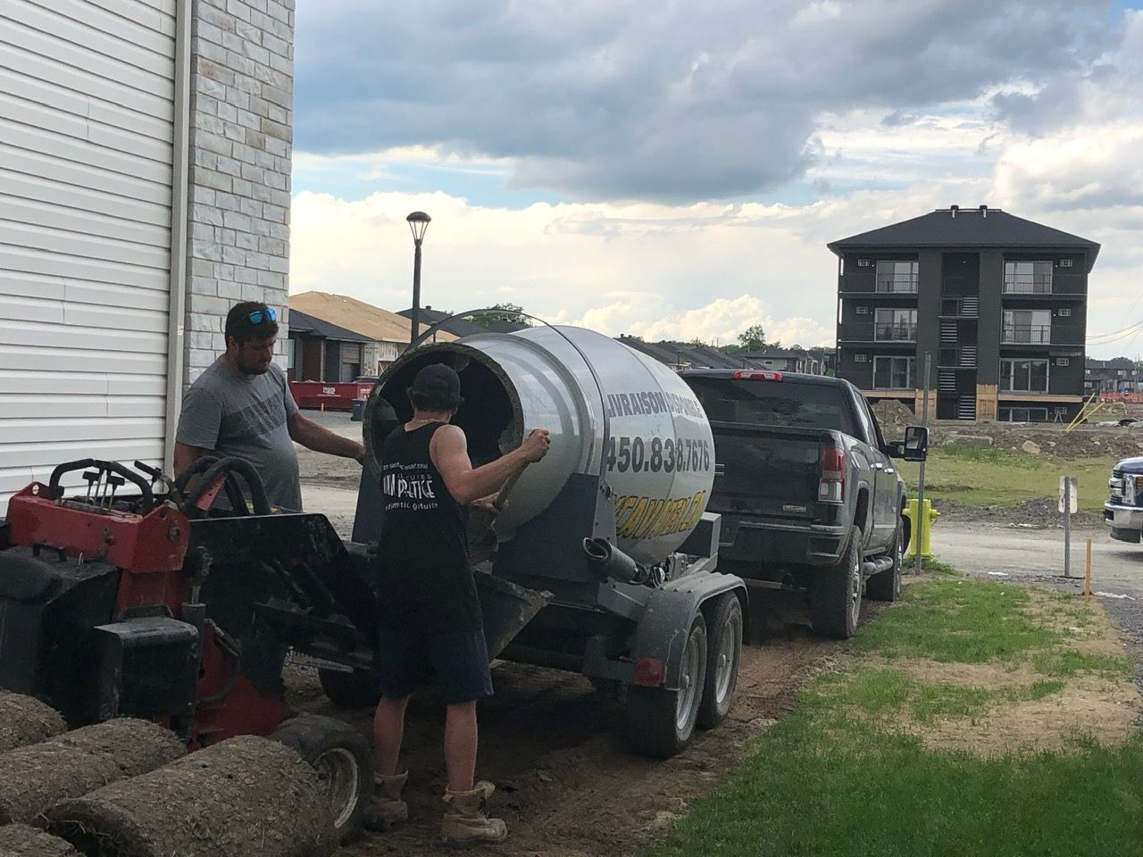Deux hommes travaillent sur une bétonnière devant une maison.