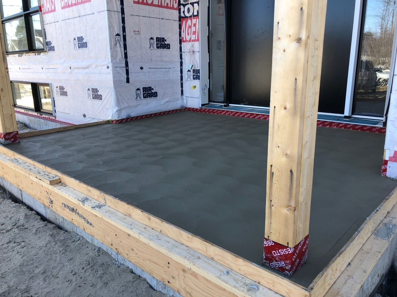 Patio en béton fraîchement coulé avec supports en bois, prêt à être construit.