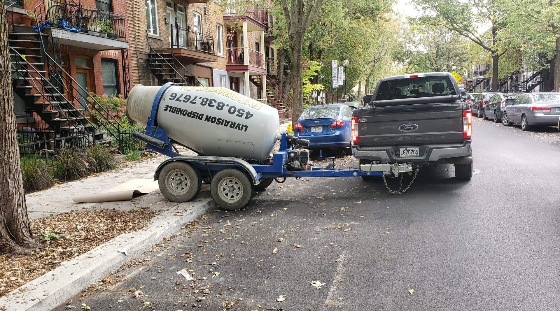 Une camionnette noire tractant une remorque bétonnière dans une rue résidentielle.
