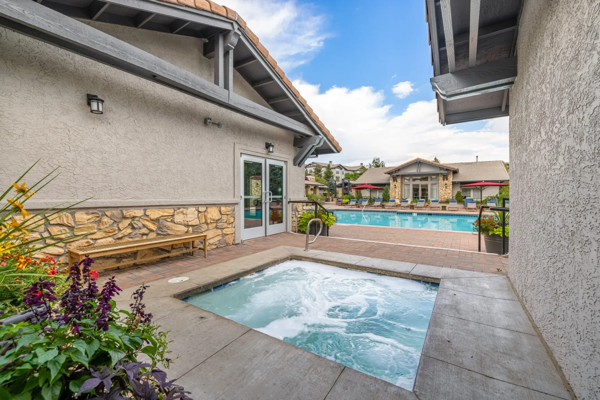 Outdoor community pool and hot tub with lounge chairs and a building in the background.