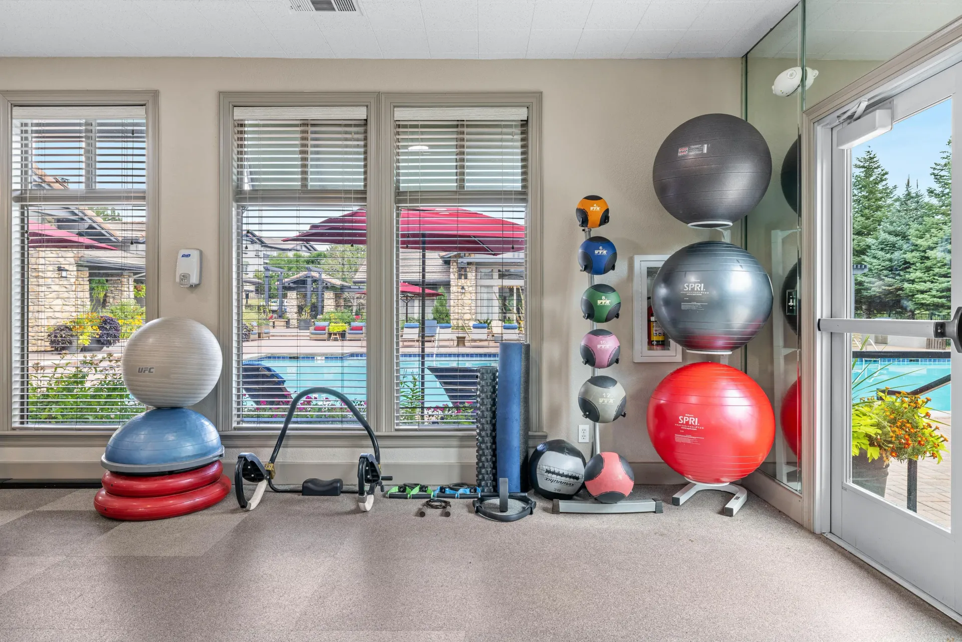 Fitness room with medicine balls, stability balls, and mats by large windows overlooking the pool.