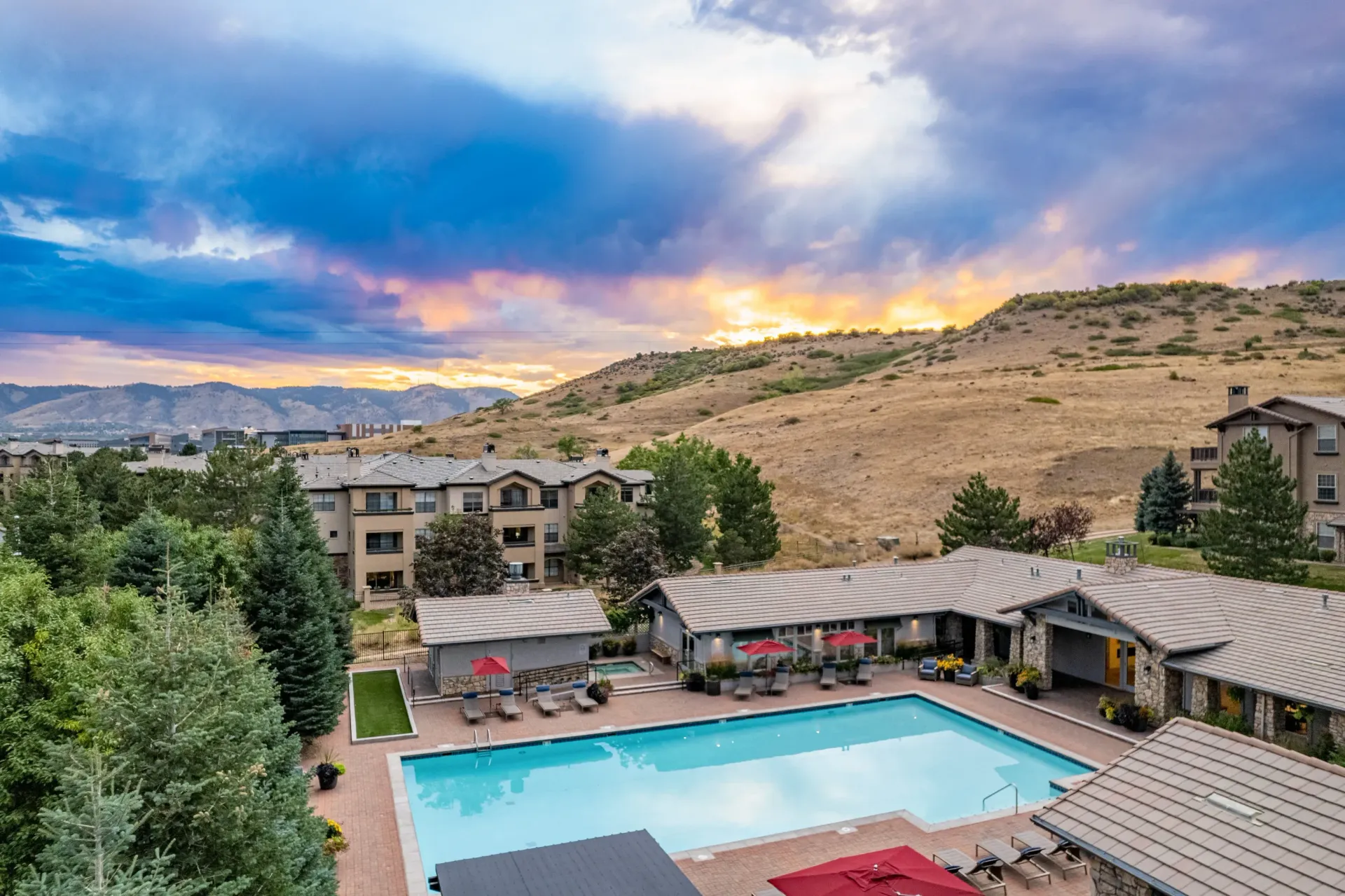 Aerial view of an apartment community pool with lounge chairs, surrounding buildings, and a hillside.