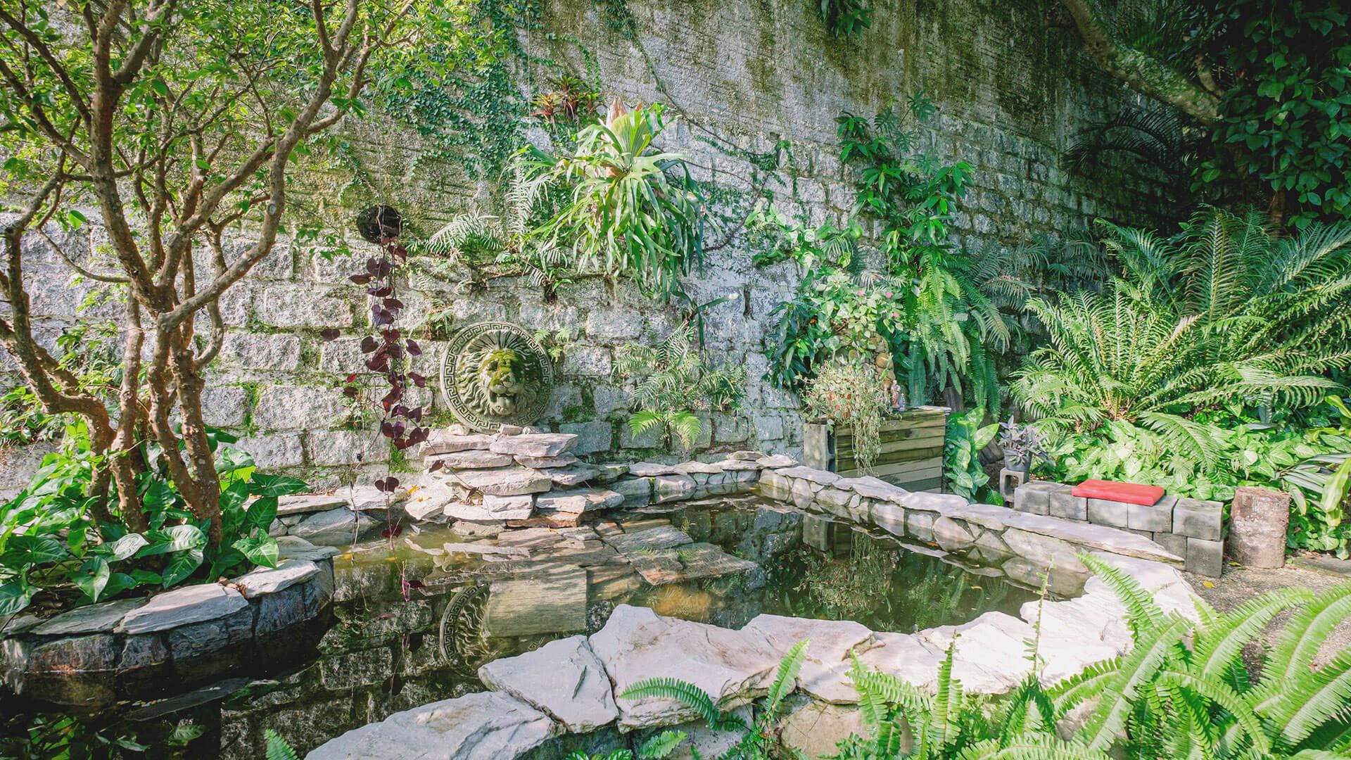 Há um lago no meio do jardim cercado por árvores e plantas.