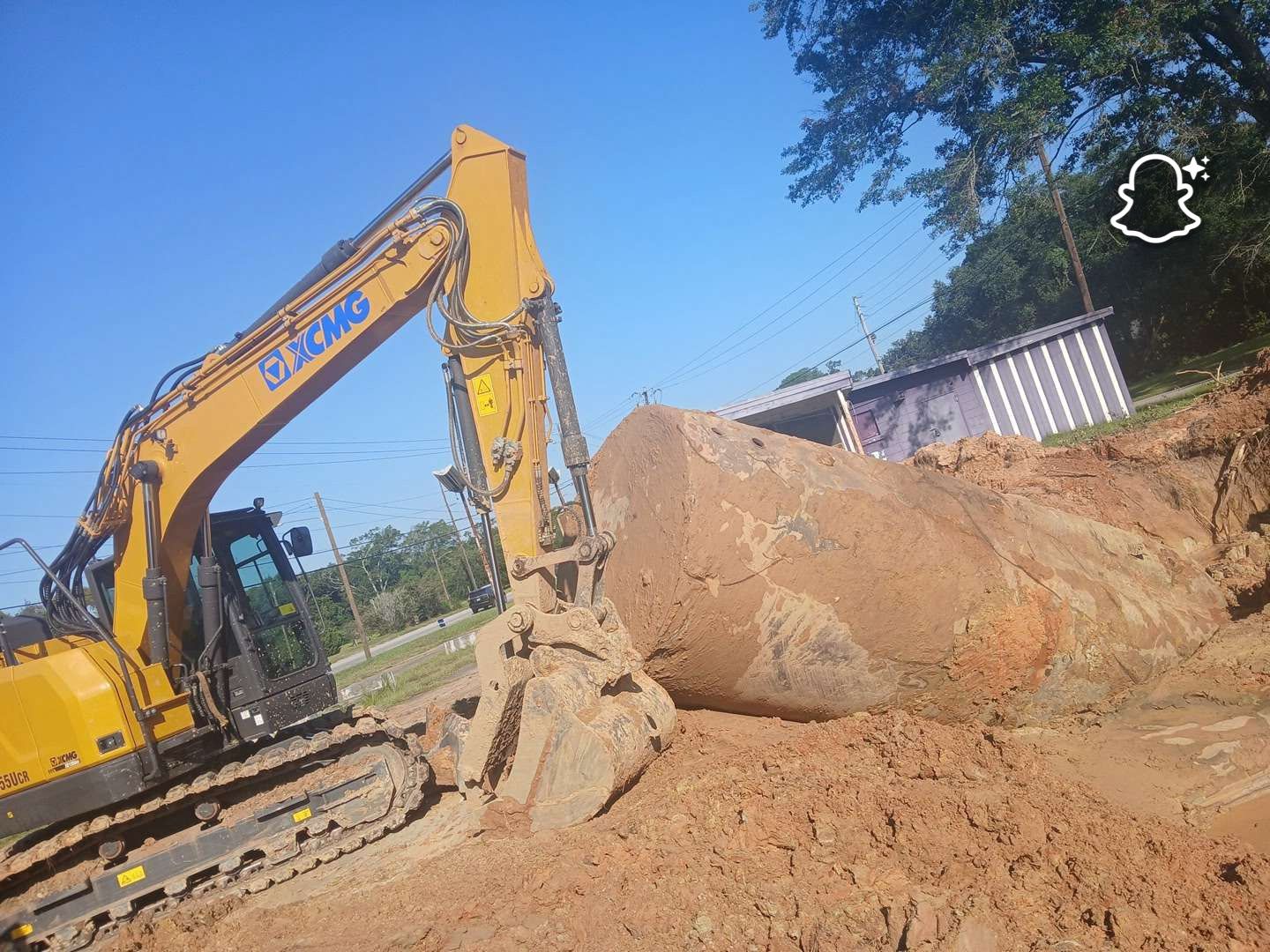 Yellow excavator digging dirt beside a house on a sunny day