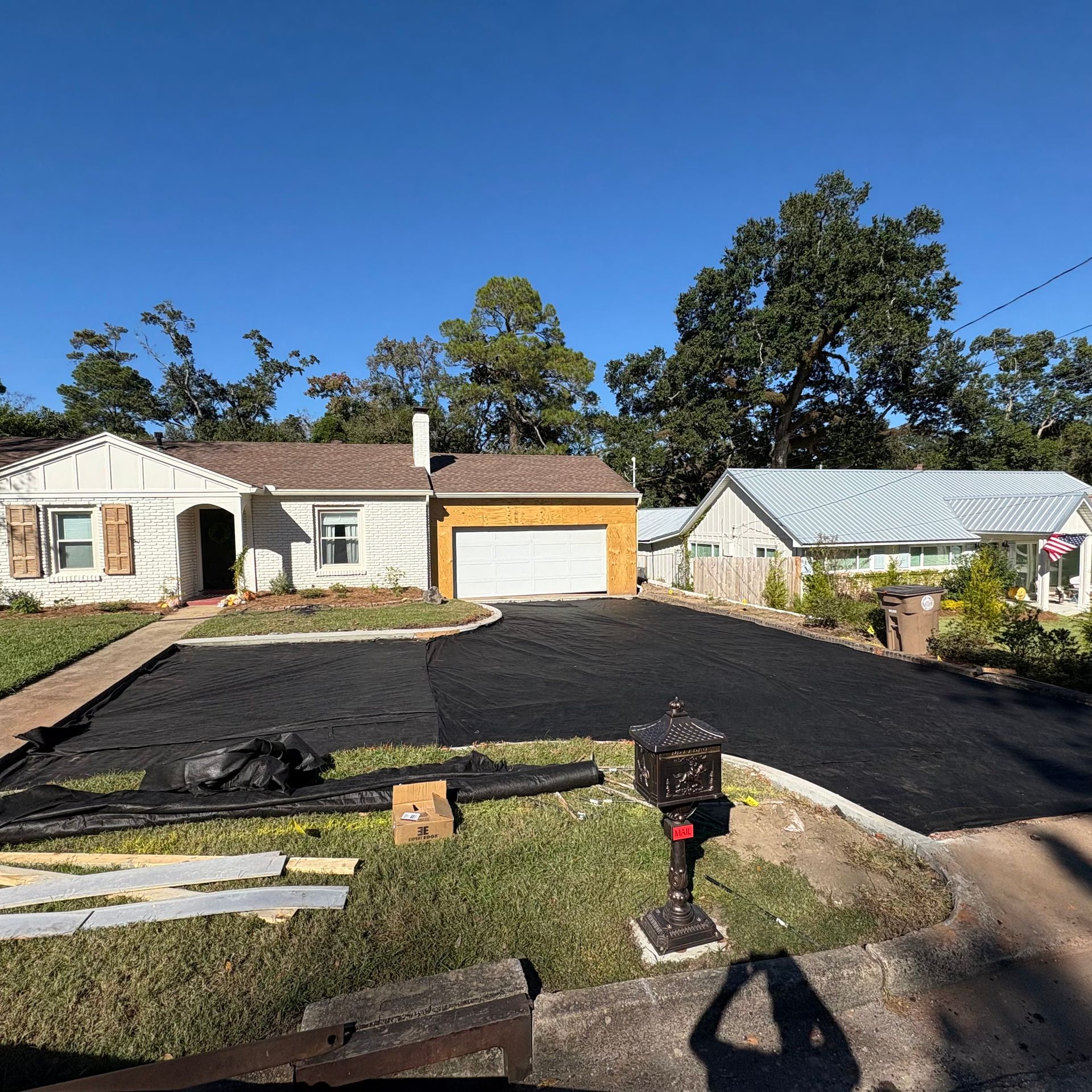 House exterior with fresh black driveway, detached garage, and mailbox under a clear blue sky