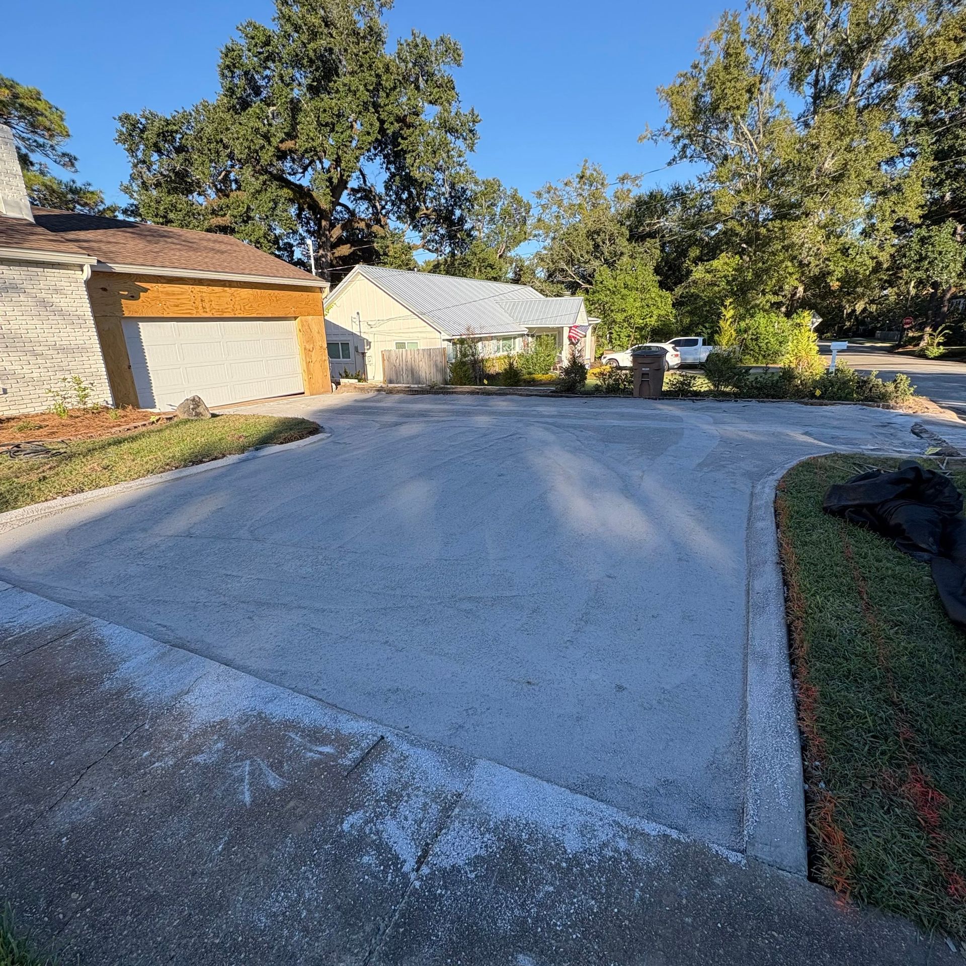 Driveway leading to a garage and trees in a suburban neighborhood under a clear blue sky