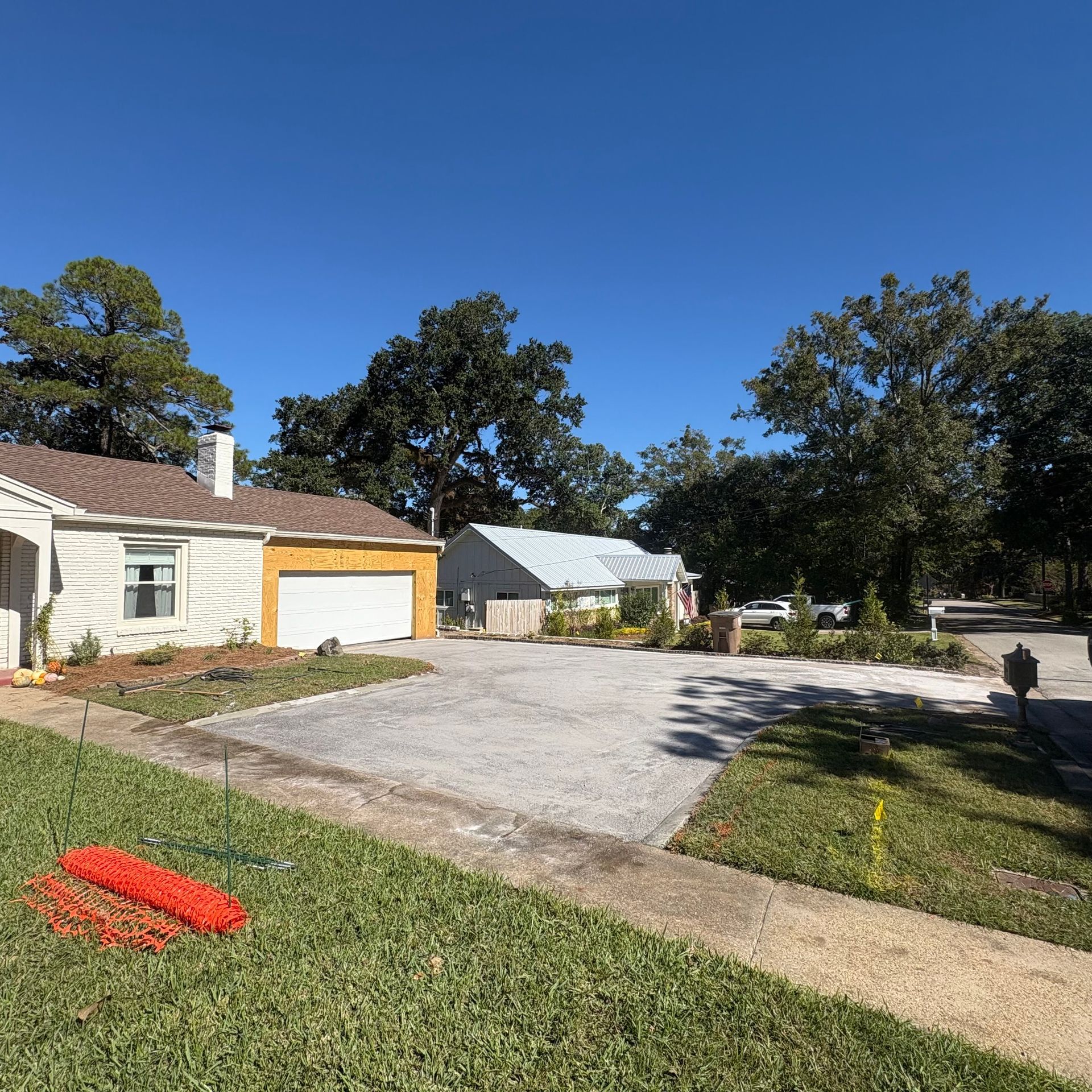 Suburban driveway beside a house and garage, with trees and a clear blue sky.