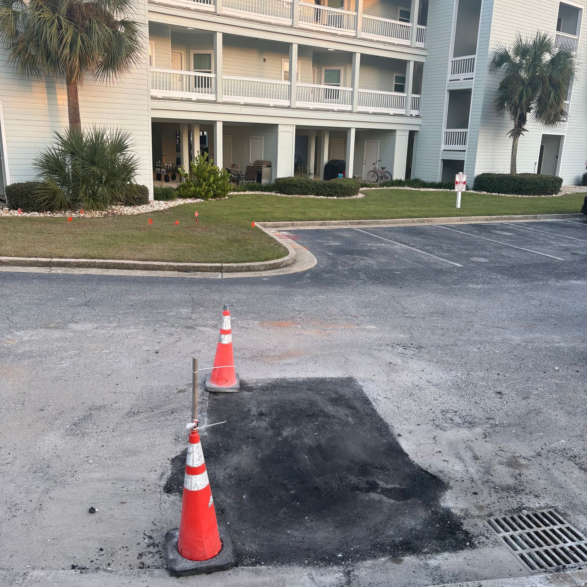 Two orange cones marking a dark asphalt patch in a parking lot beside an apartment building.