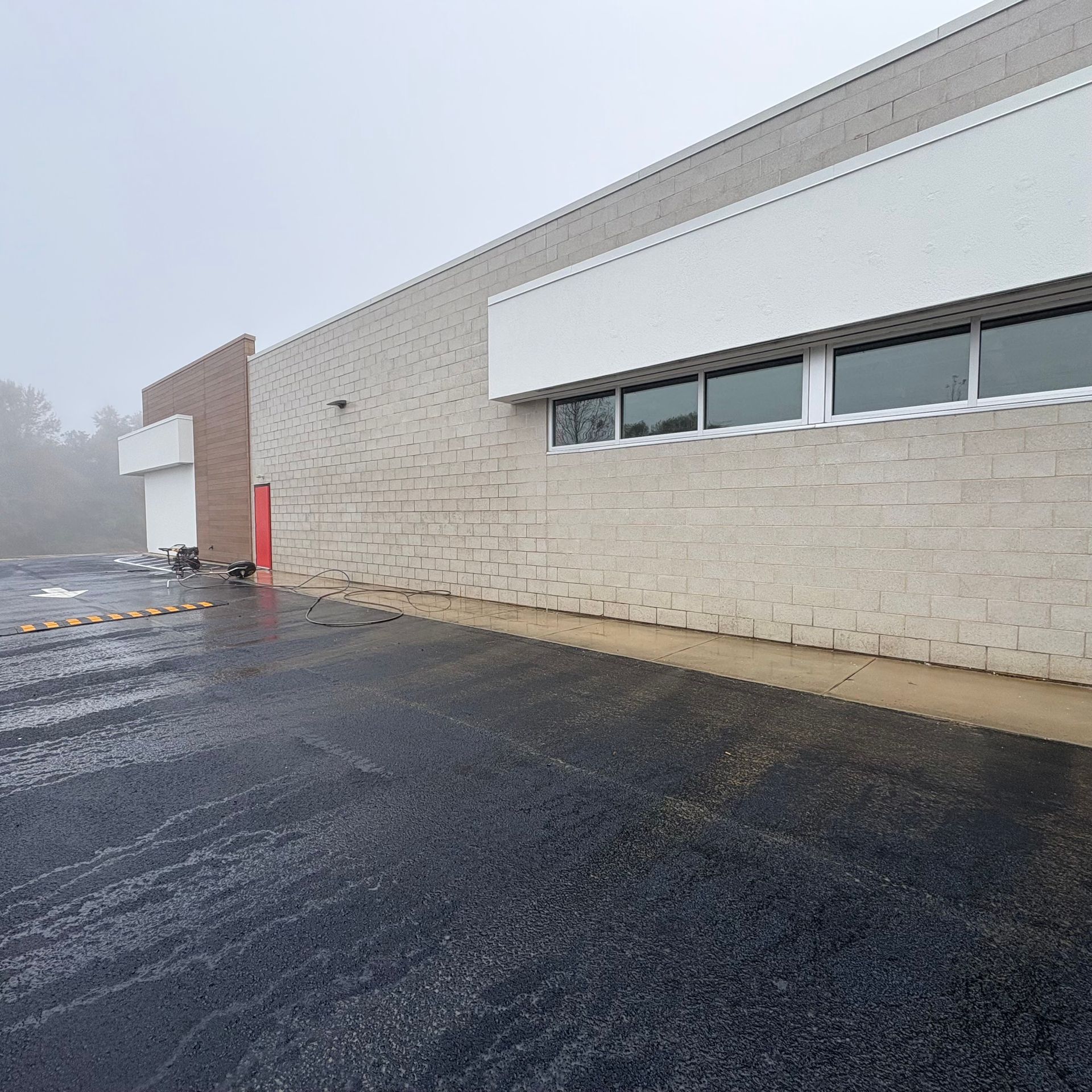 Foggy exterior of a white commercial building with a red door and wet asphalt parking lot