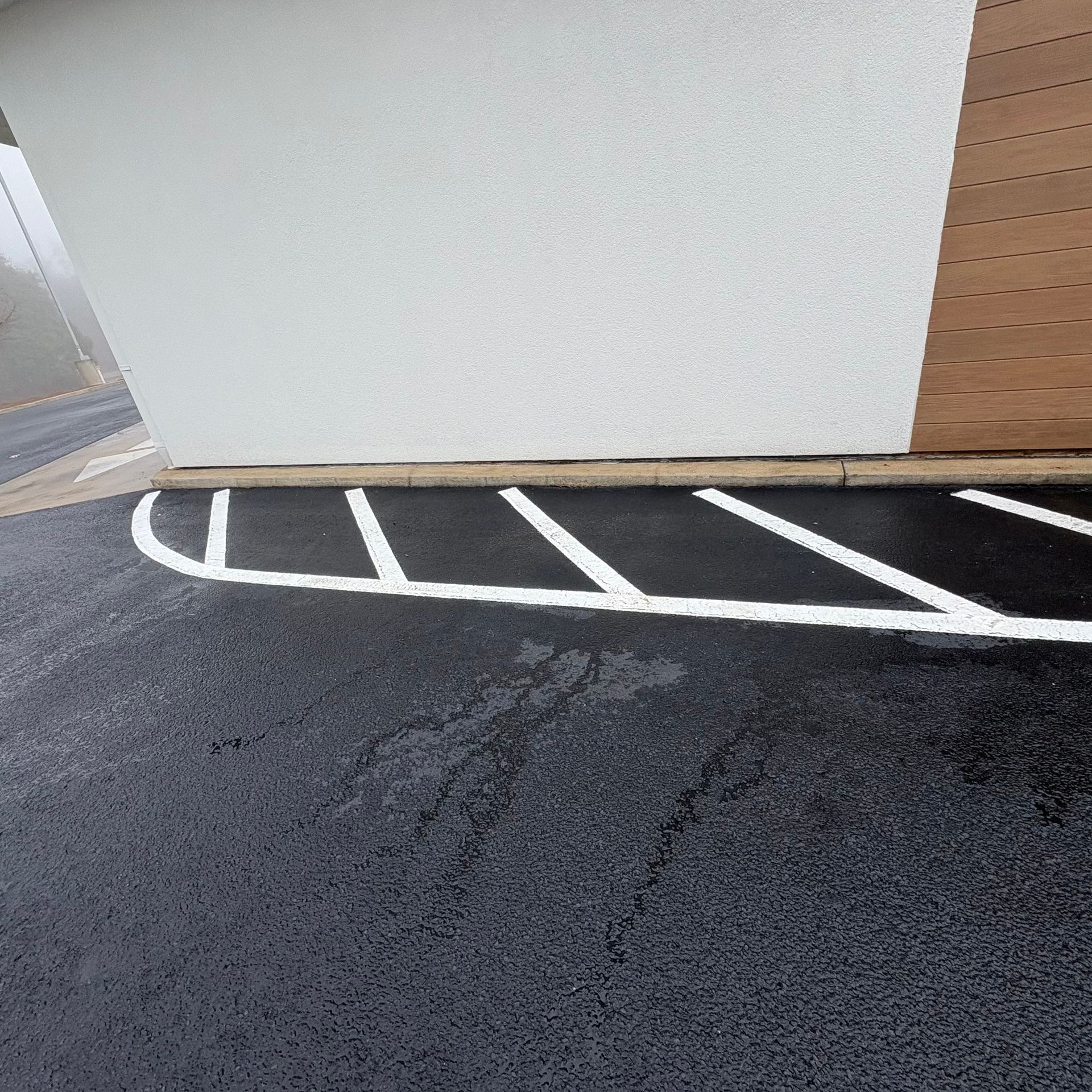 White building edge beside a black asphalt lot with white painted parking lines and tan wood siding
