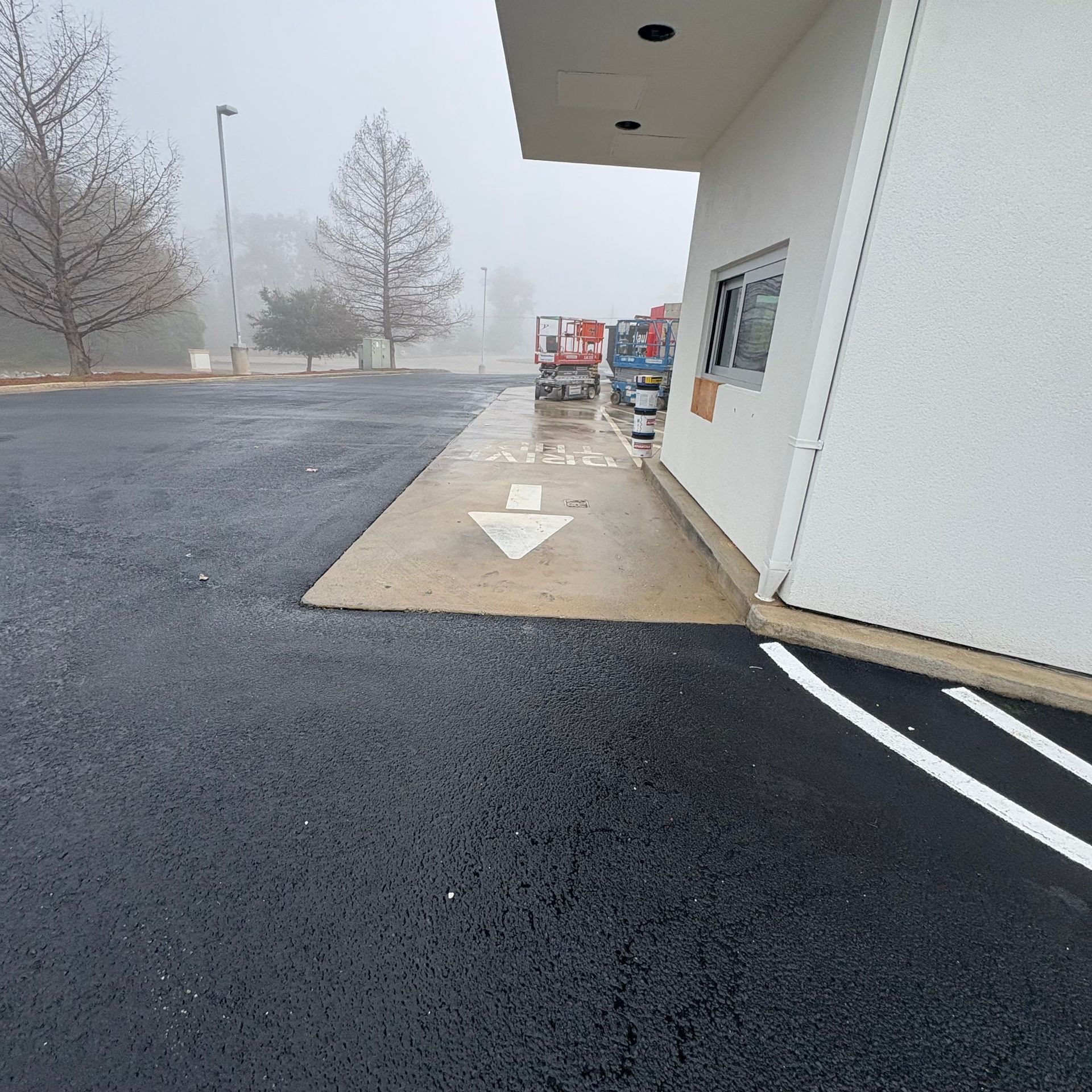 Foggy parking lot beside a white building, with a wet asphalt drive and shopping carts near the entrance.