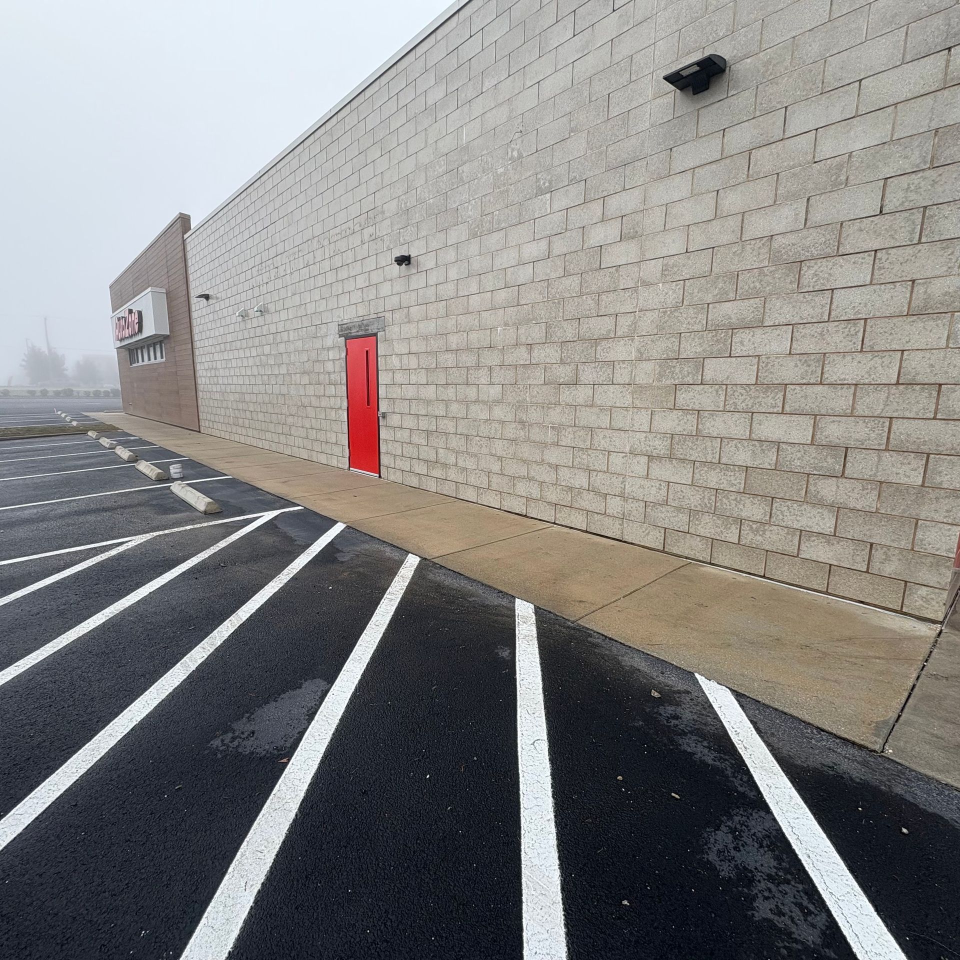 Empty parking lot beside a beige brick building with a red door and white diagonal pavement lines.