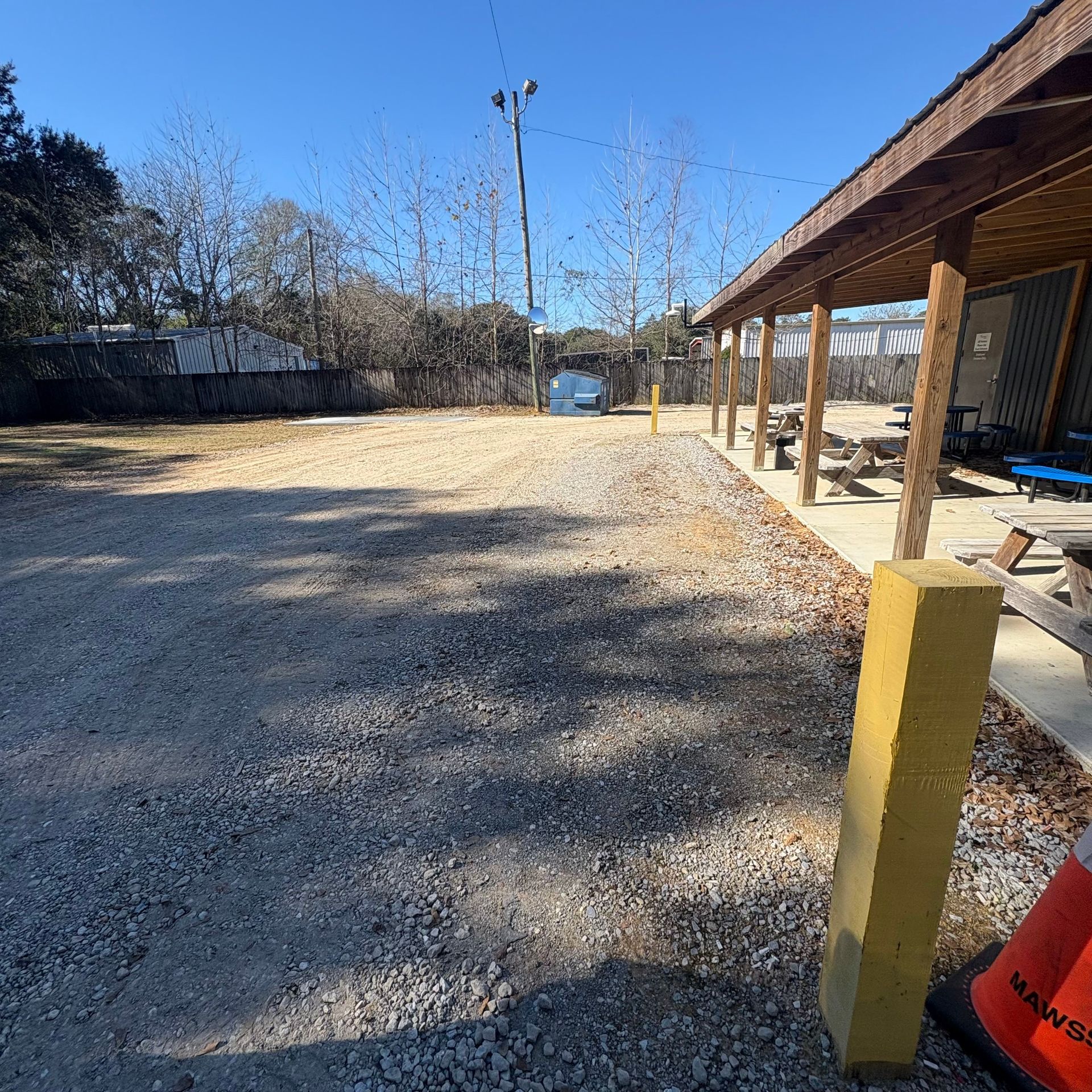 Gravel lot beside a covered patio, with yellow bollard and blue sky in the background