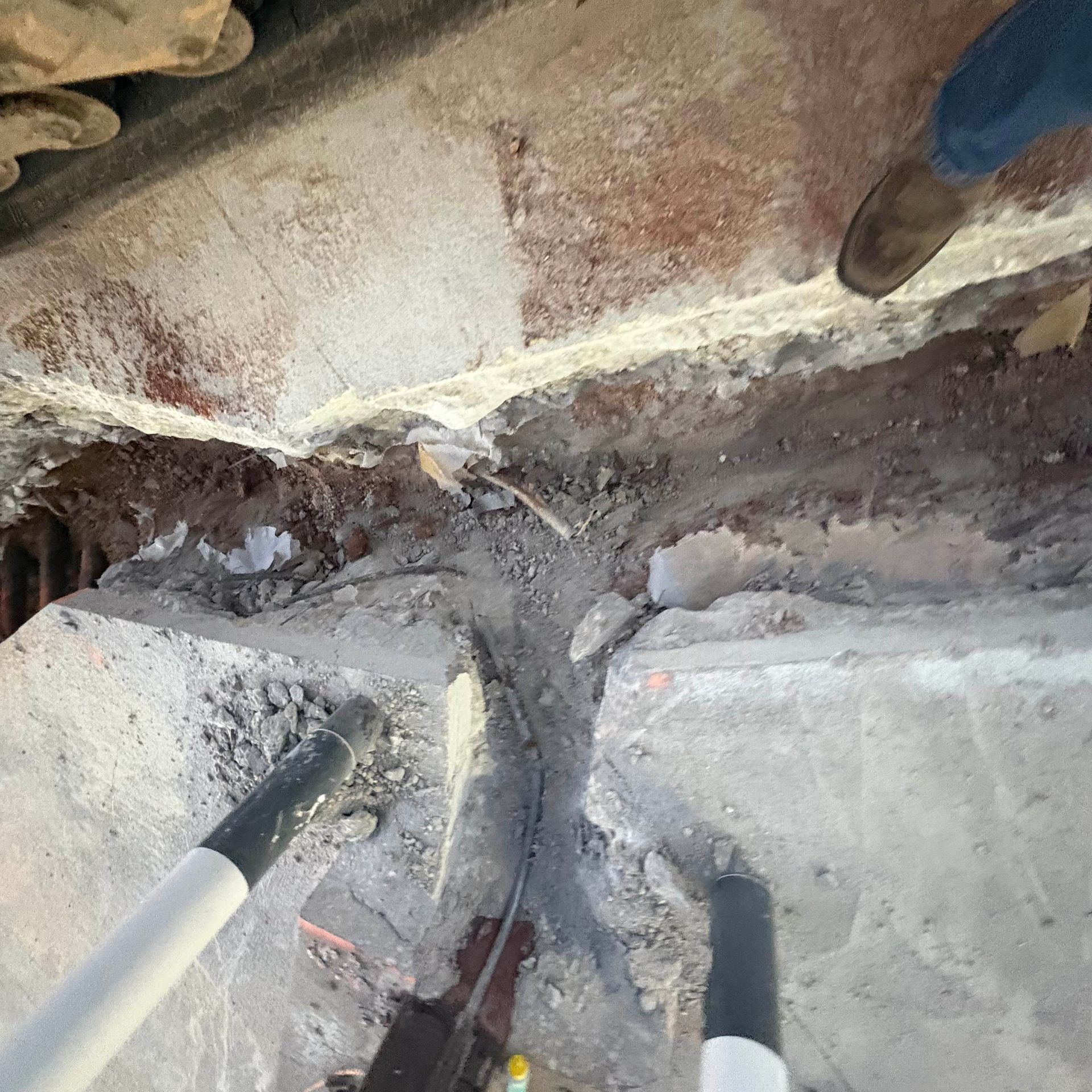 Two shovels digging into a dusty concrete crevice under a damaged surface