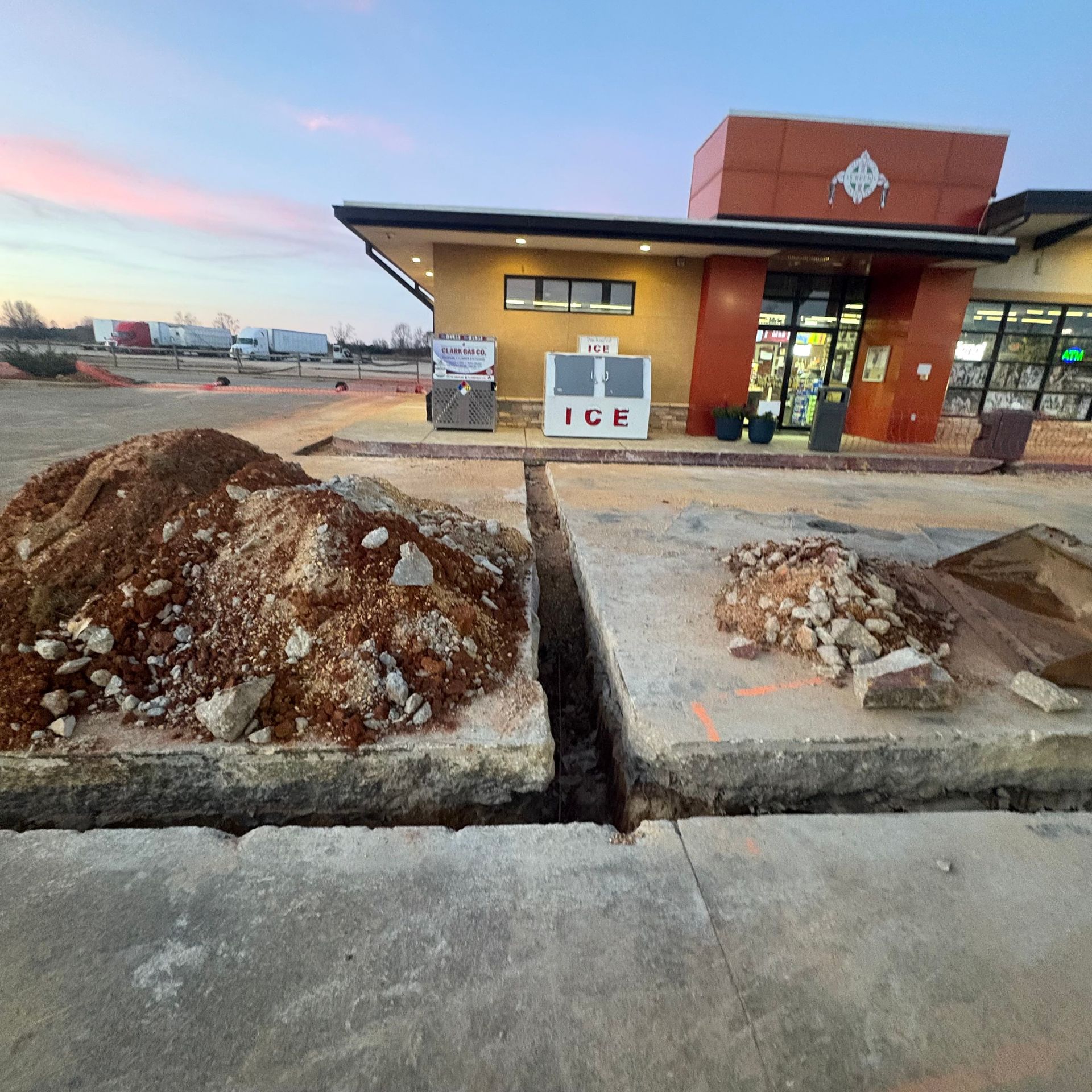 Gas station convenience store at dusk with dirt and rock piles in the foreground
