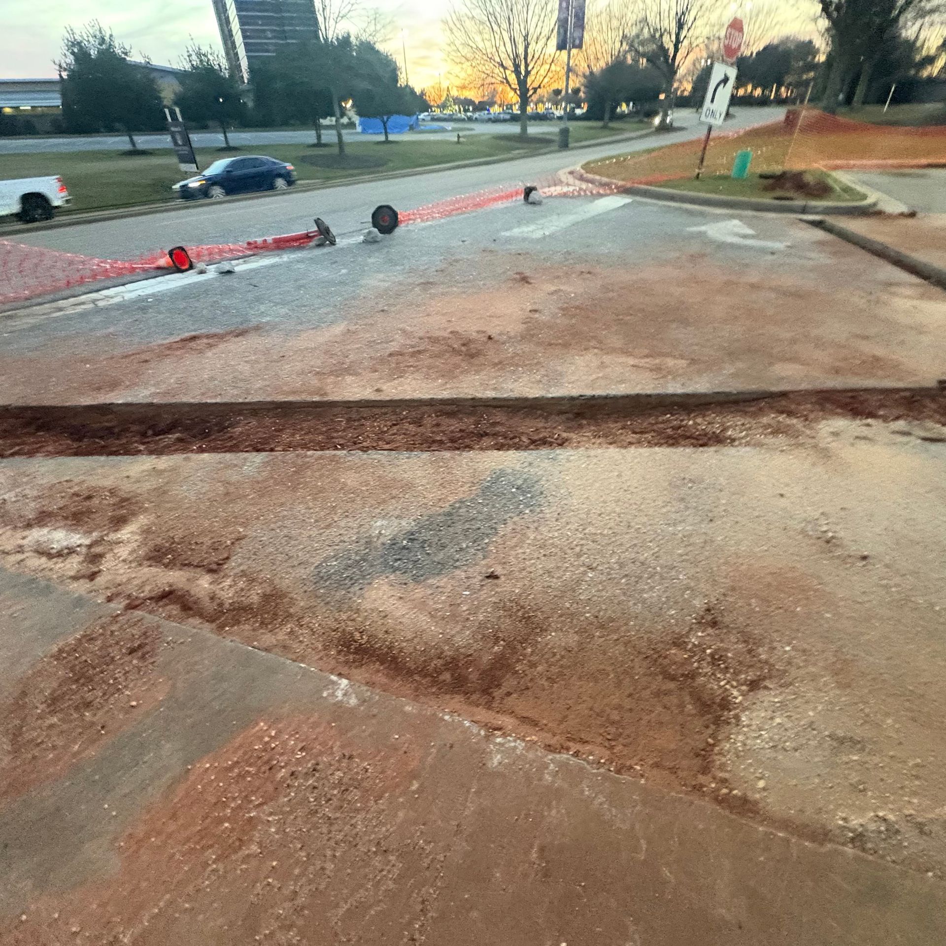 Broken curb ramp with cracked concrete and orange construction barrier near a street at sunset