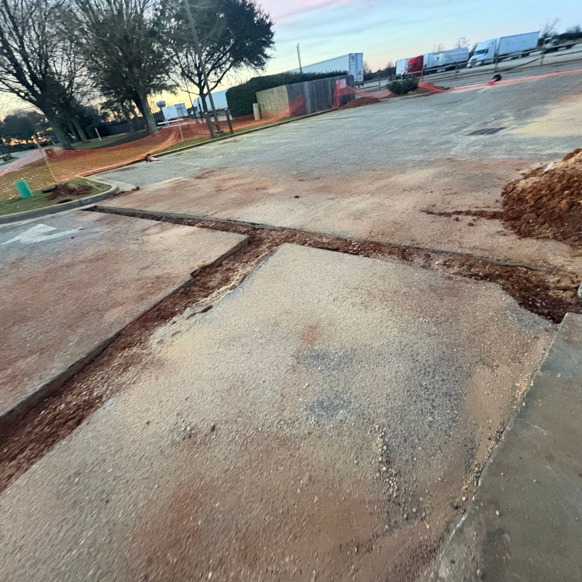 Cracked concrete slabs at a construction site with dirt, fencing, and trees in the background