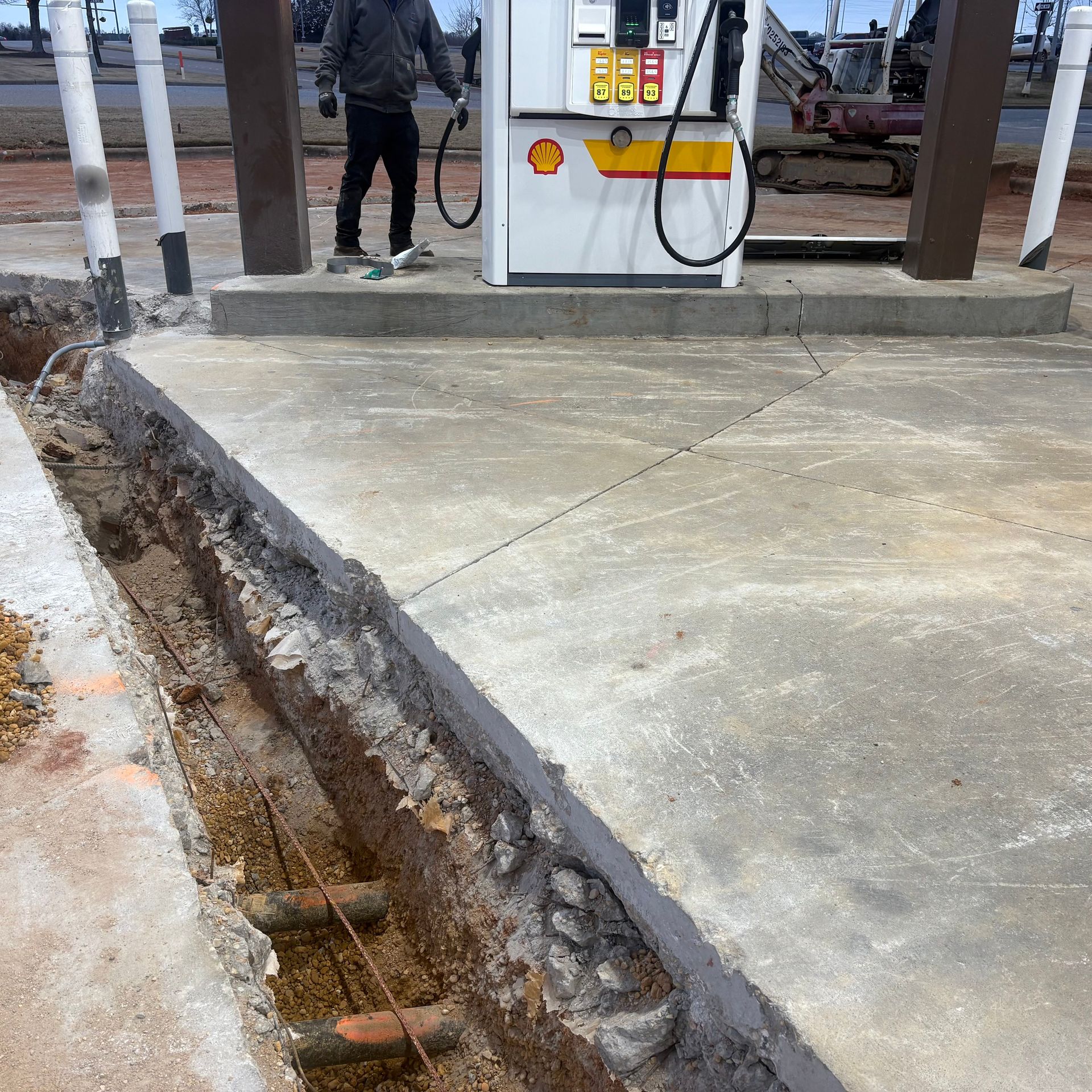 Concrete forecourt with a long open trench beside a fuel pump island at a gas station