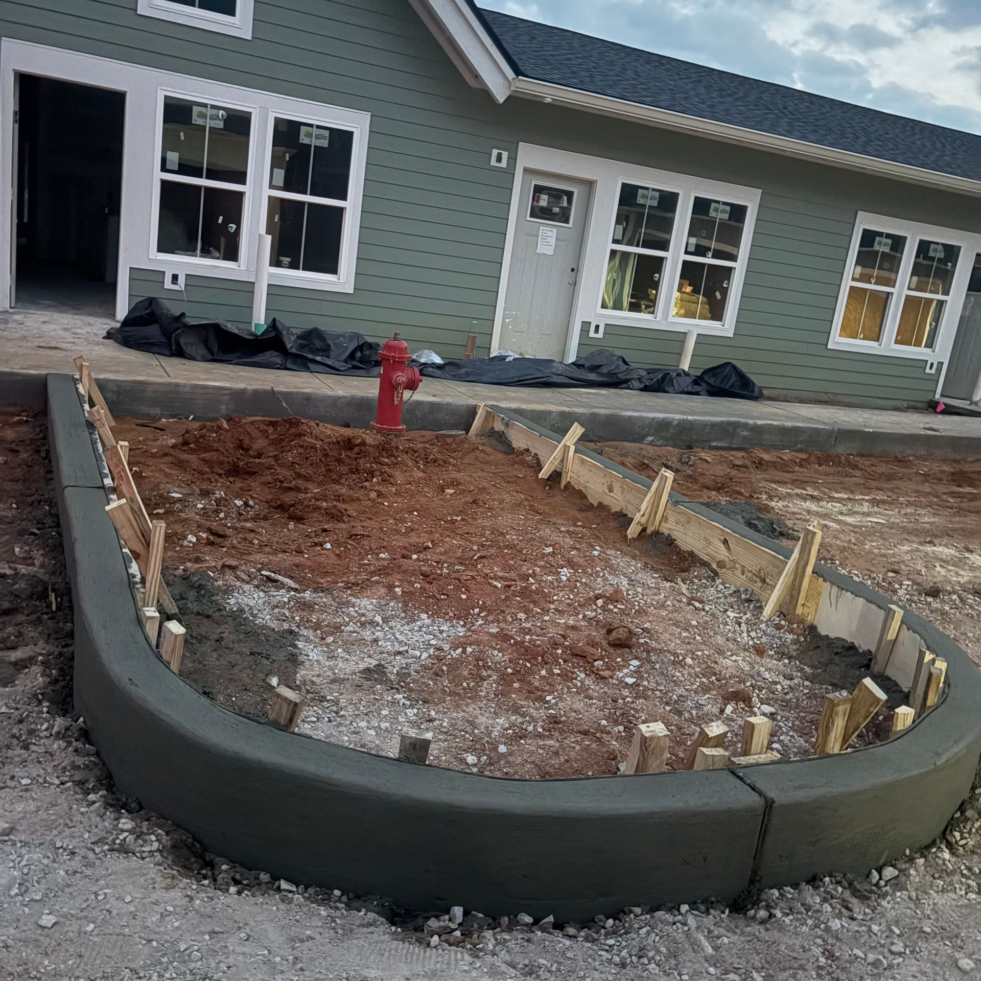 Front yard construction with a curved concrete border, dirt fill, and a red fire hydrant in front of a house.