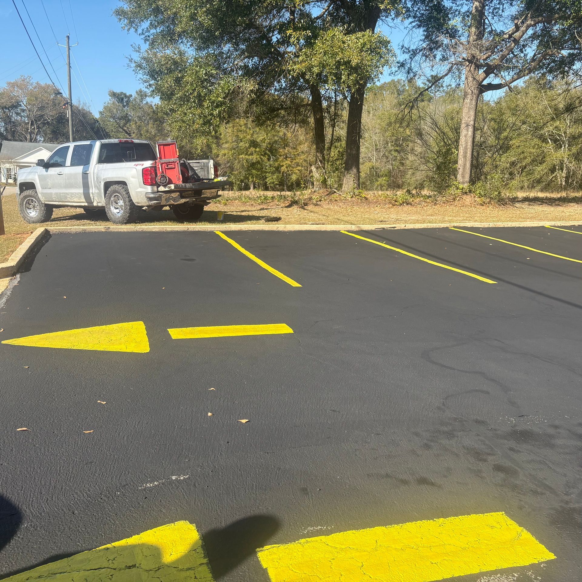 Parking lot with bright yellow directional arrows and a white pickup truck near trees and a utility pole.
