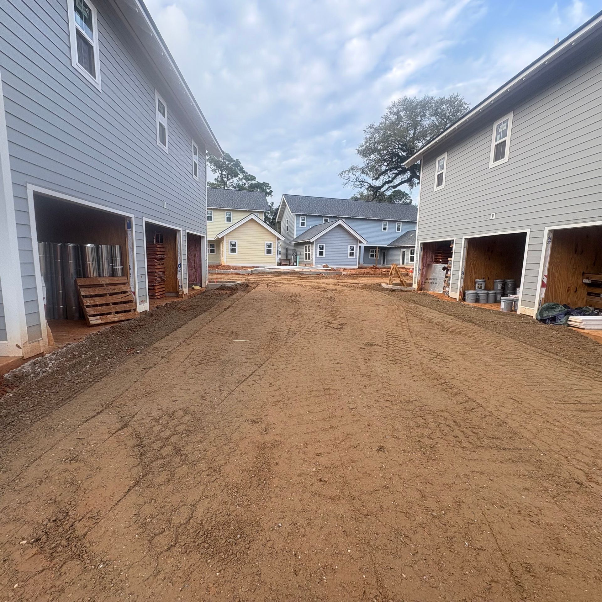 Dirt driveway between two gray apartment buildings under construction, with houses visible in the background.