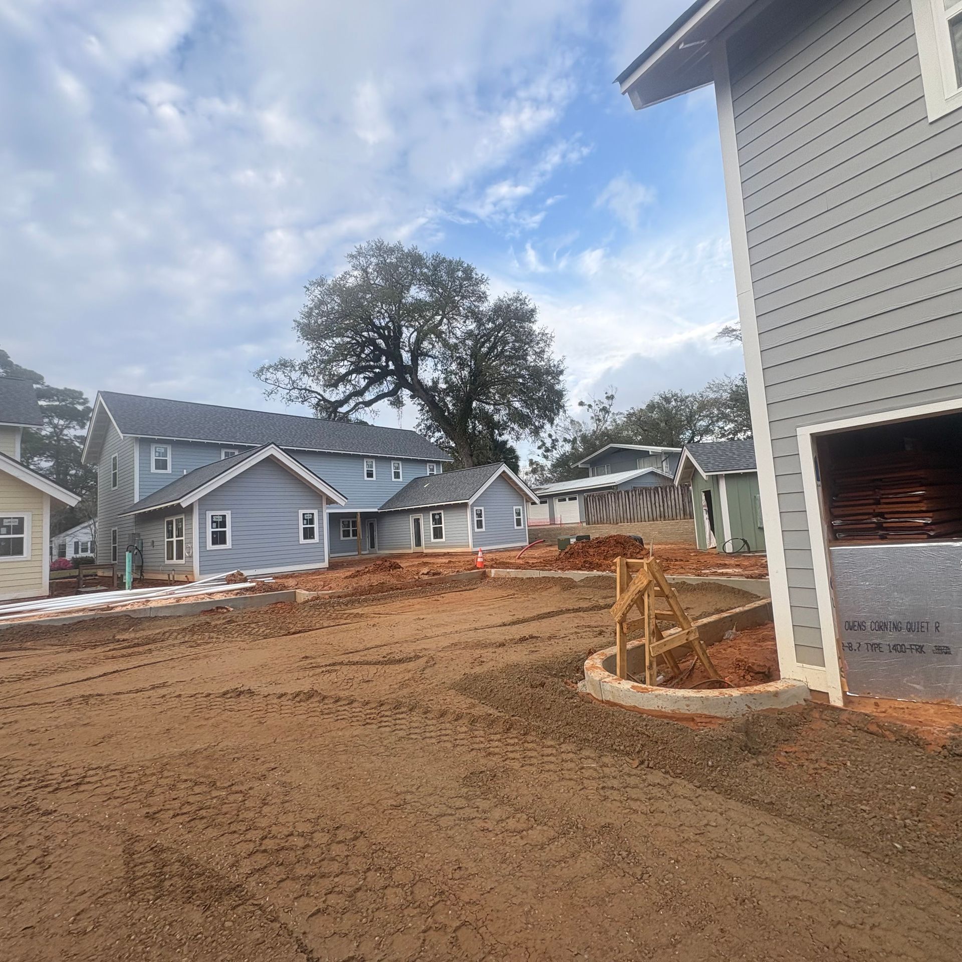 New house construction site with graded dirt lot, houses in background, and a garage wall on the right