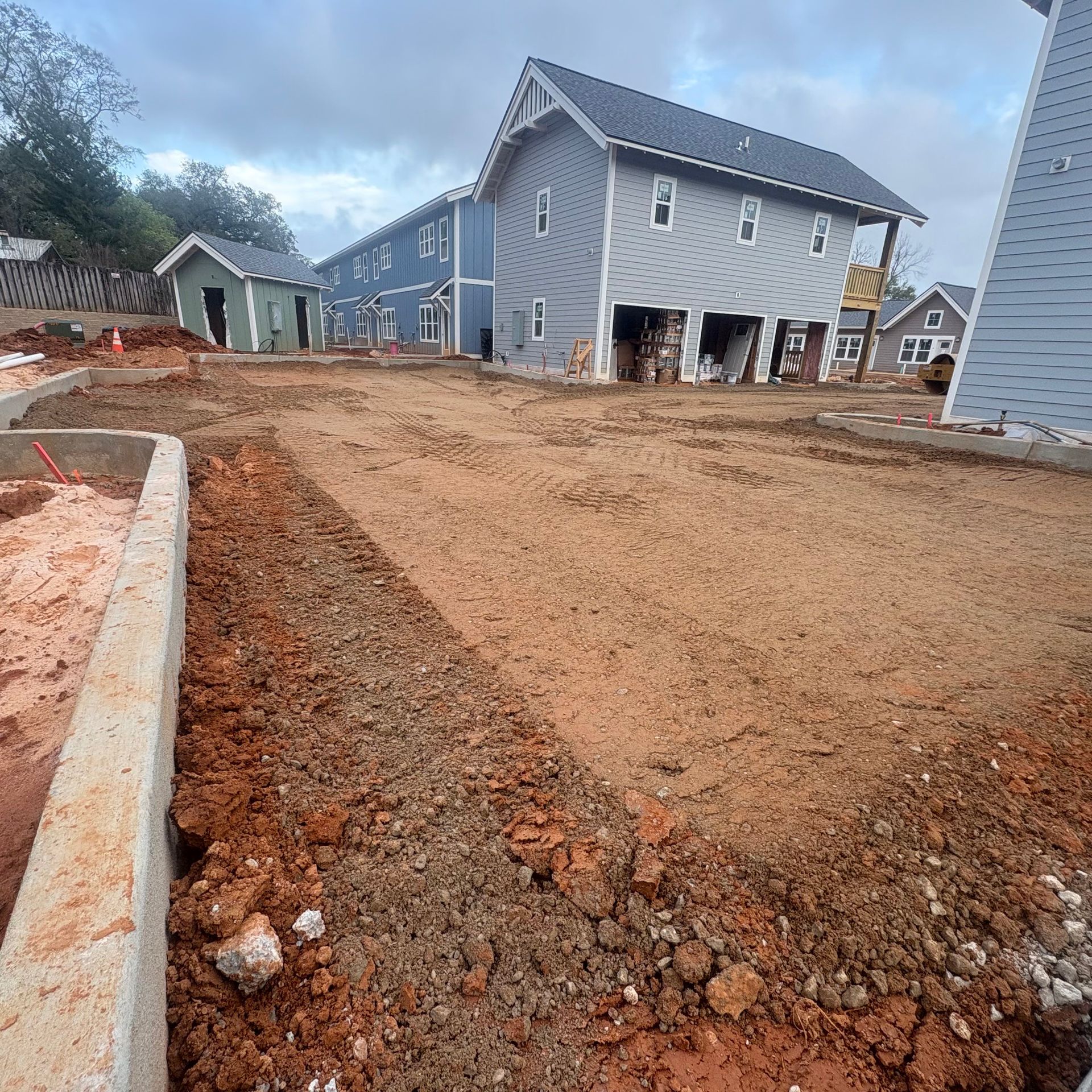 New house construction site with graded dirt lot and blue-gray homes in the background