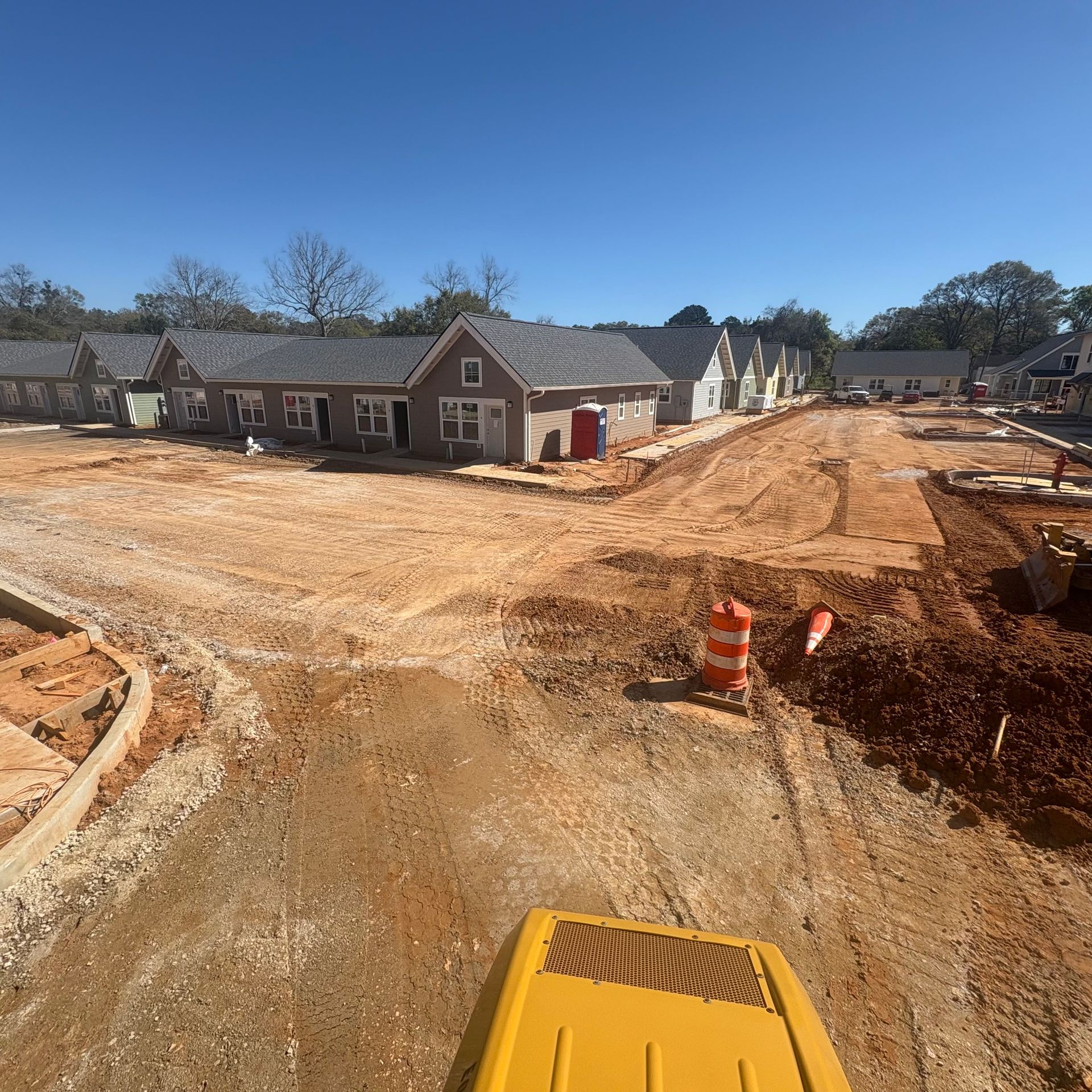 Construction site with dirt roads and a row of houses under a clear blue sky