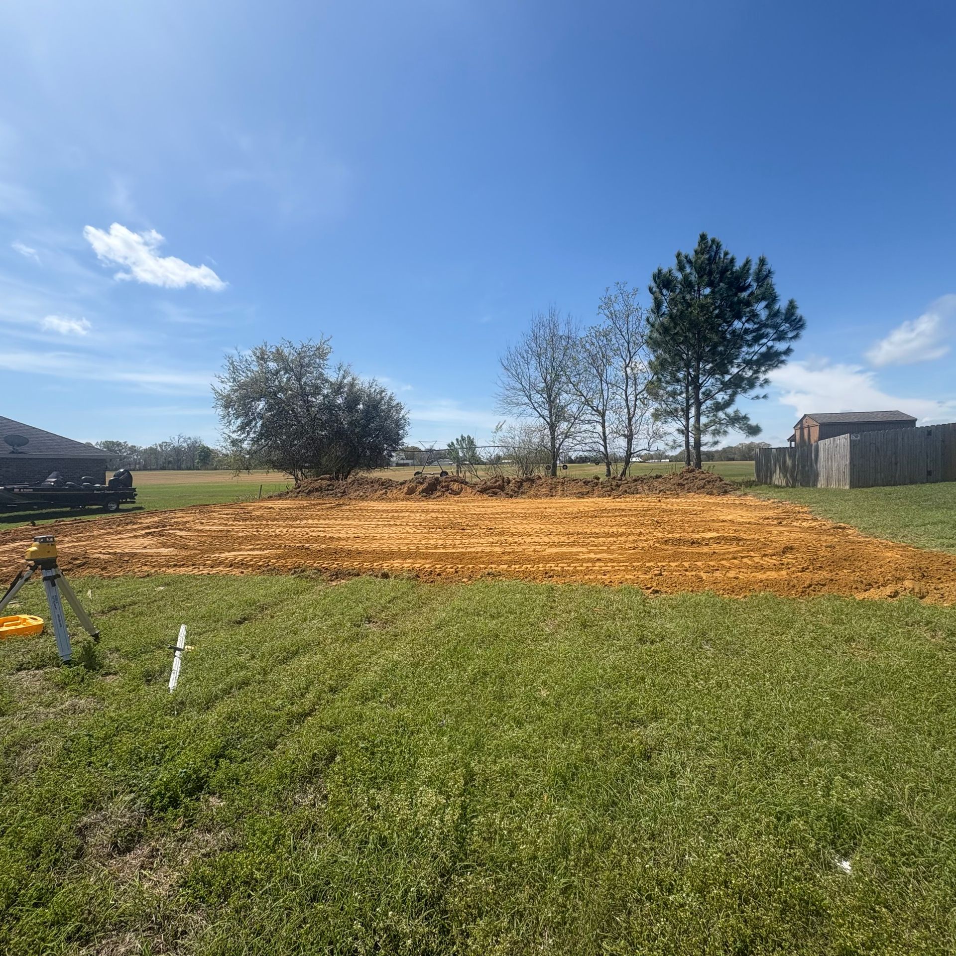 Backyard with a freshly spread orange-brown mulch bed under a blue sky, bordered by grass and trees
