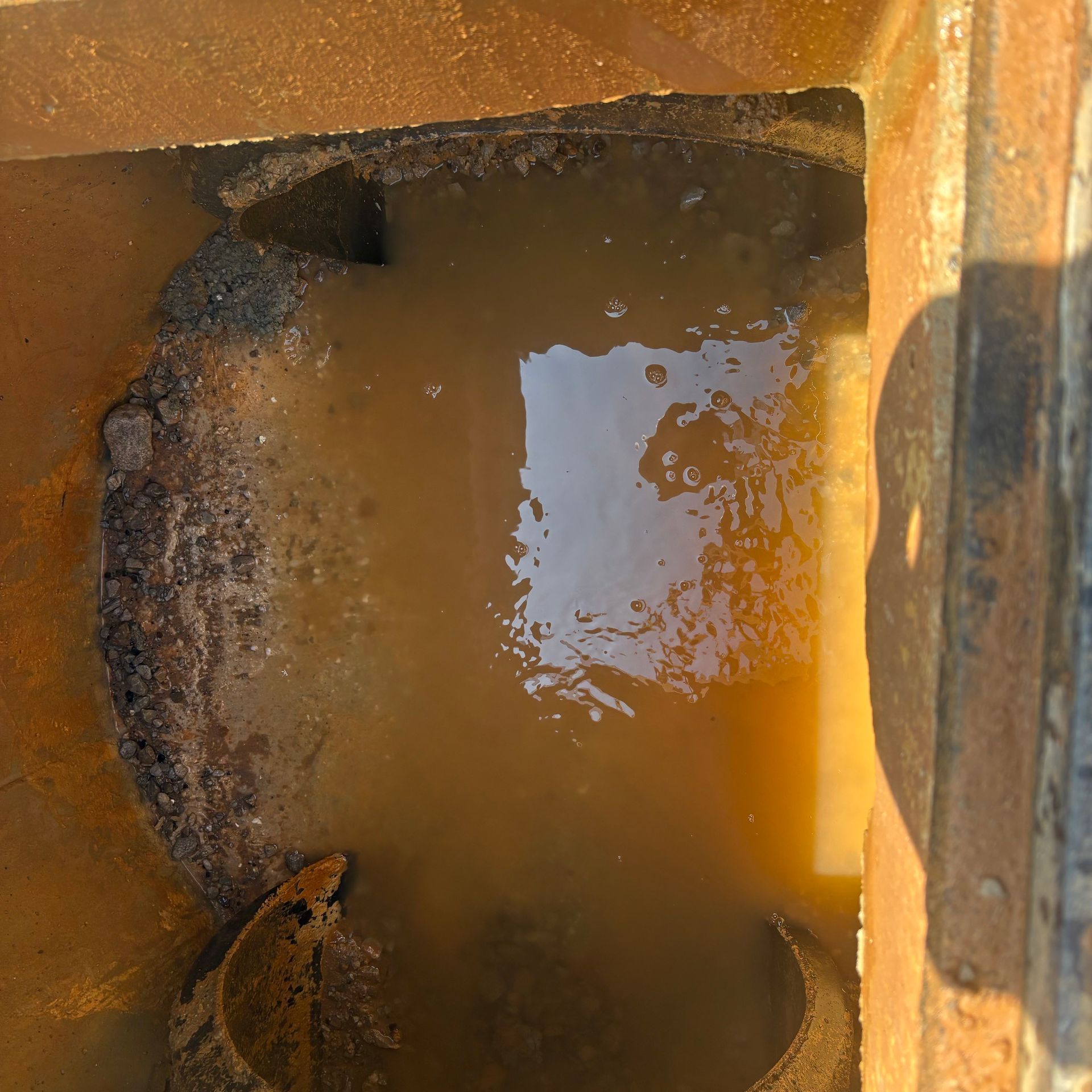 Rusty metal hatch with murky brown water and a bright reflection in the center
